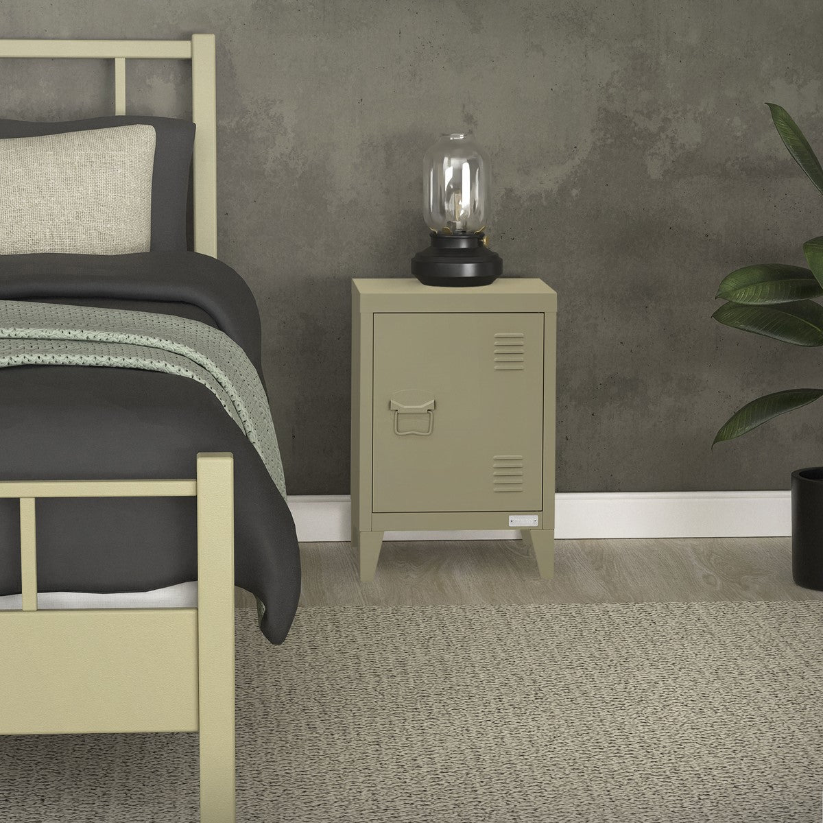 Olive-green bedside table with a lamp and a bed in the background.