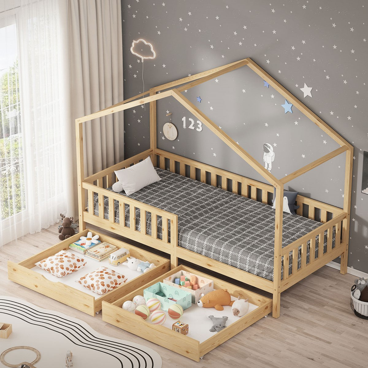 Holz-Kinderbett in Hausform mit Schubladen, grauer Bettwäsche und Kissen; daneben liegen Spielzeug und Bücher.