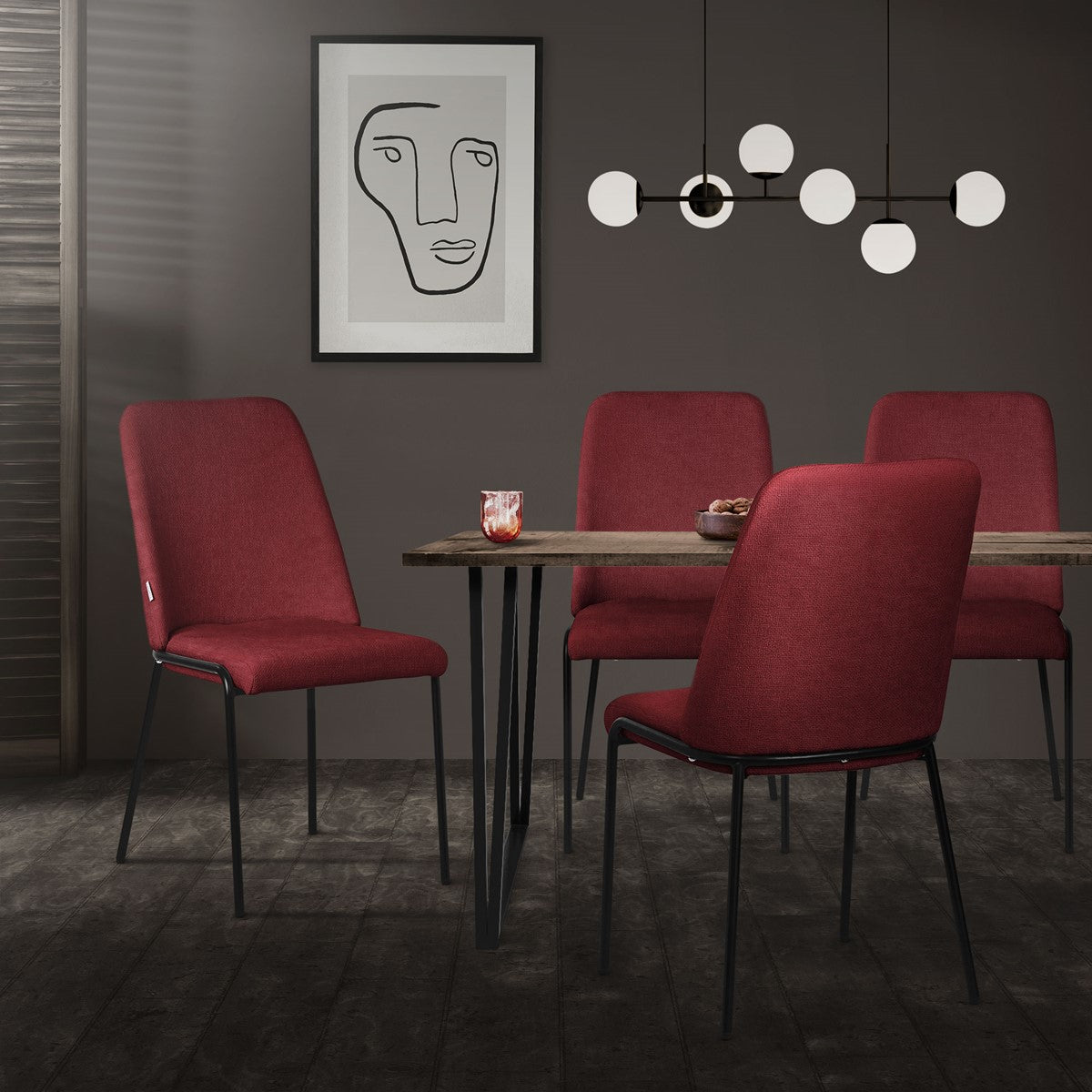 A dining area with a table and four red chairs, with an abstract picture on the wall.
