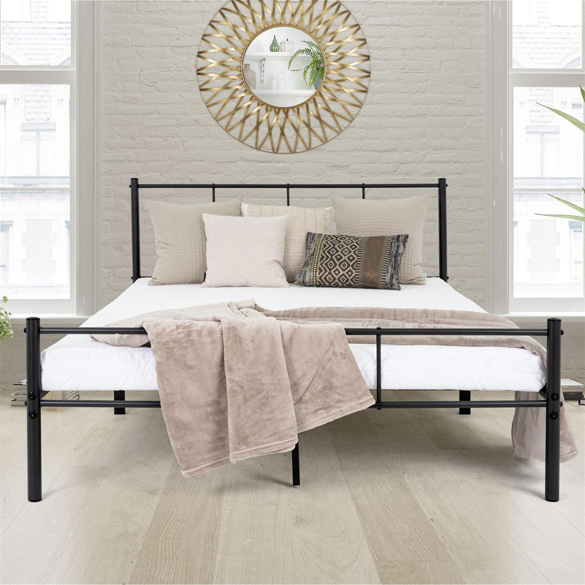 Schwarzes Metallbett mit weißer Bettwäsche, beigen Kissen und Decke vor heller Ziegelwand mit rundem goldfarbenem Spiegel.