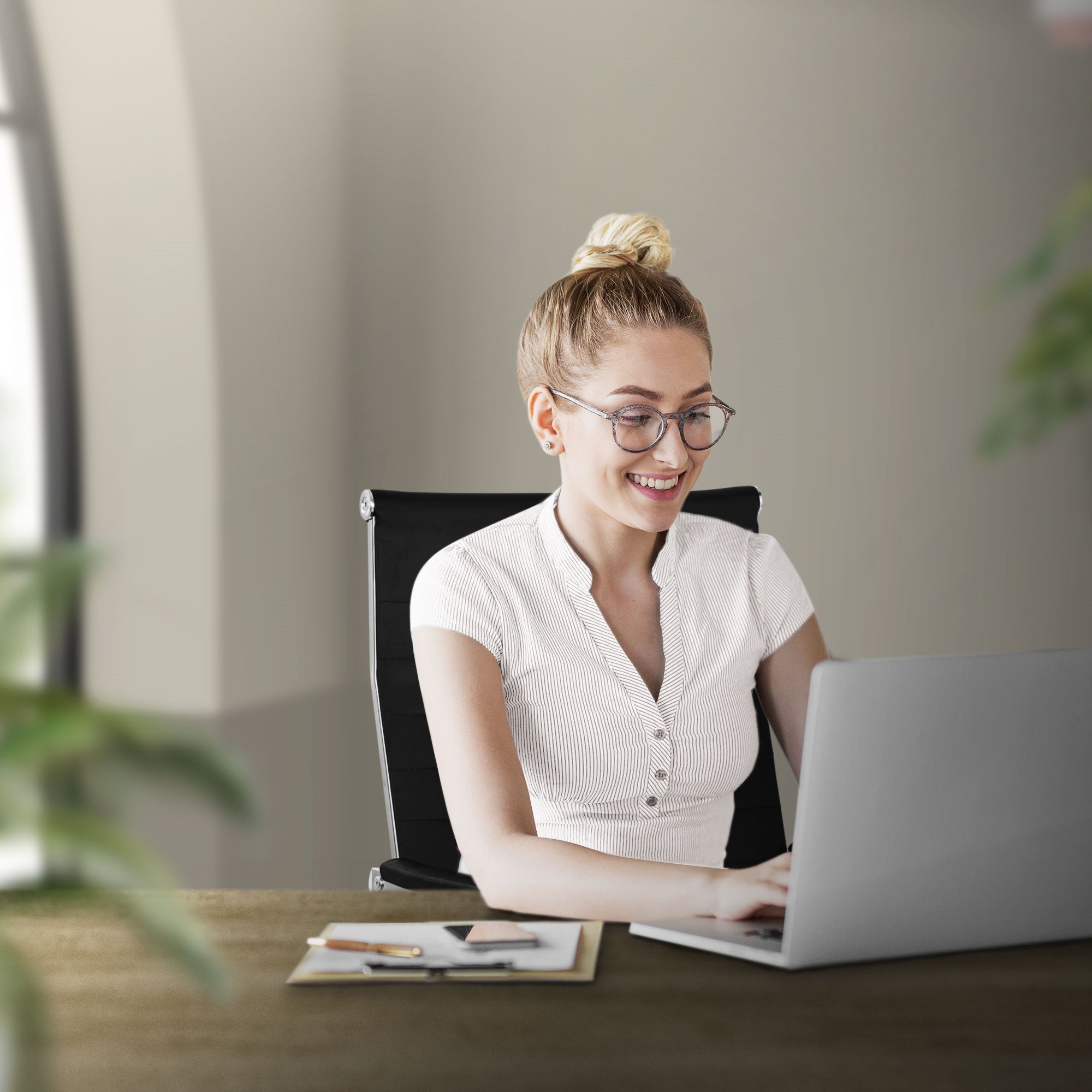 Eine lächelnde Frau mit Brille sitzt an einem Tisch und arbeitet am Laptop.
