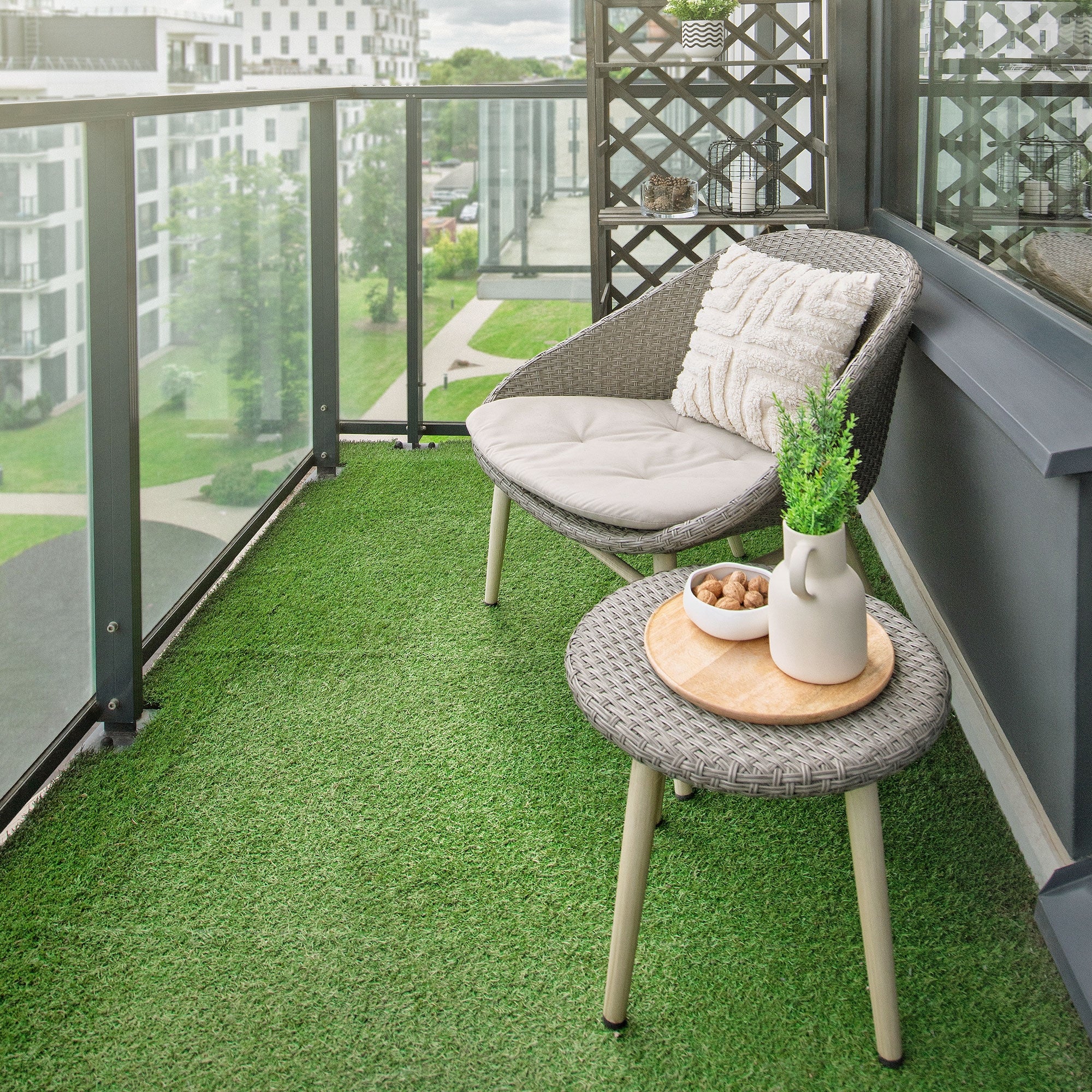 Balcone con una sedia grigia, un tavolo e una pianta su erba artificiale verde.