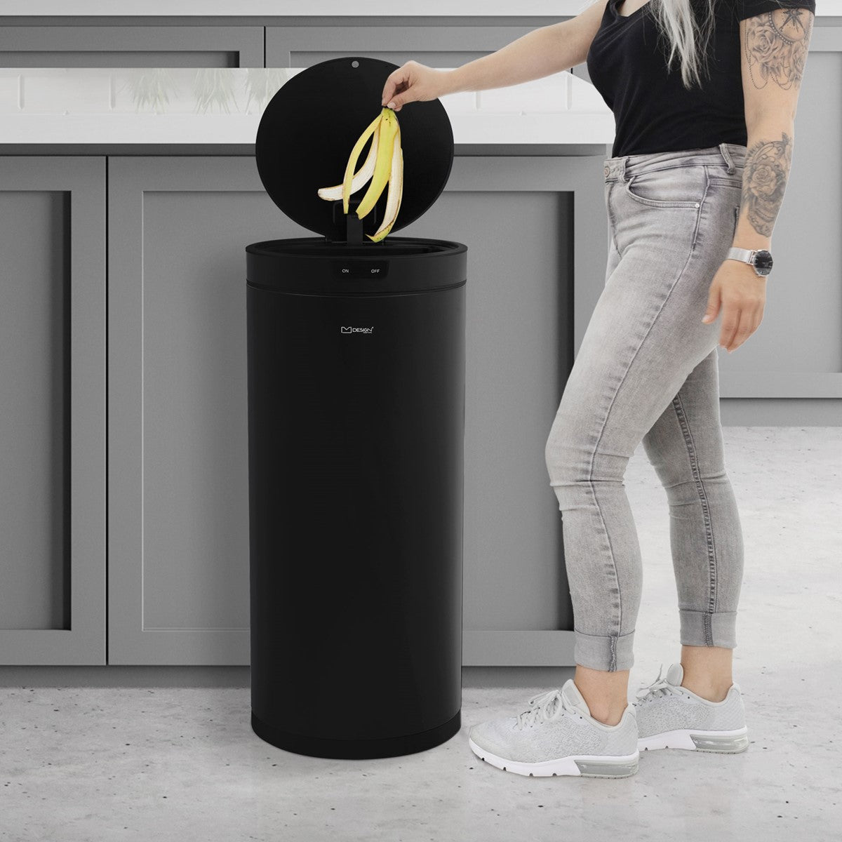 Person mit langen Haaren, die eine Banane in einen schwarzen Mülleimer wirft.