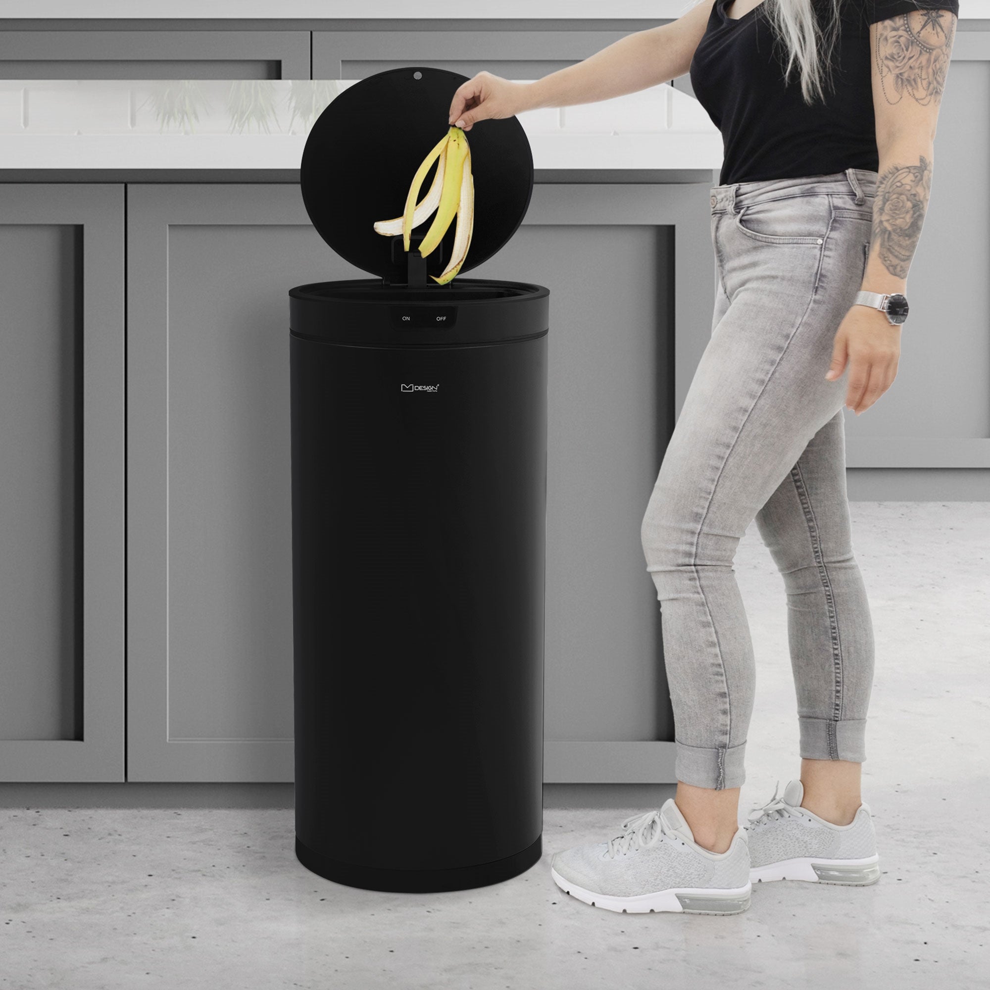 Person mit langen Haaren, die eine Banane in einen schwarzen Mülleimer wirft.