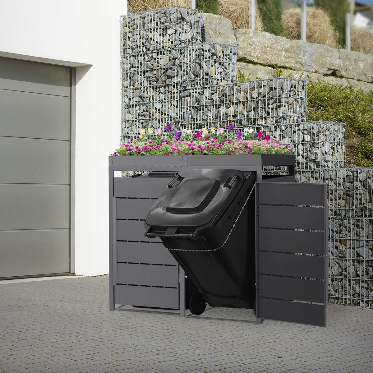 Waste container box with an open door, waste container visible, in front of a stone wall.