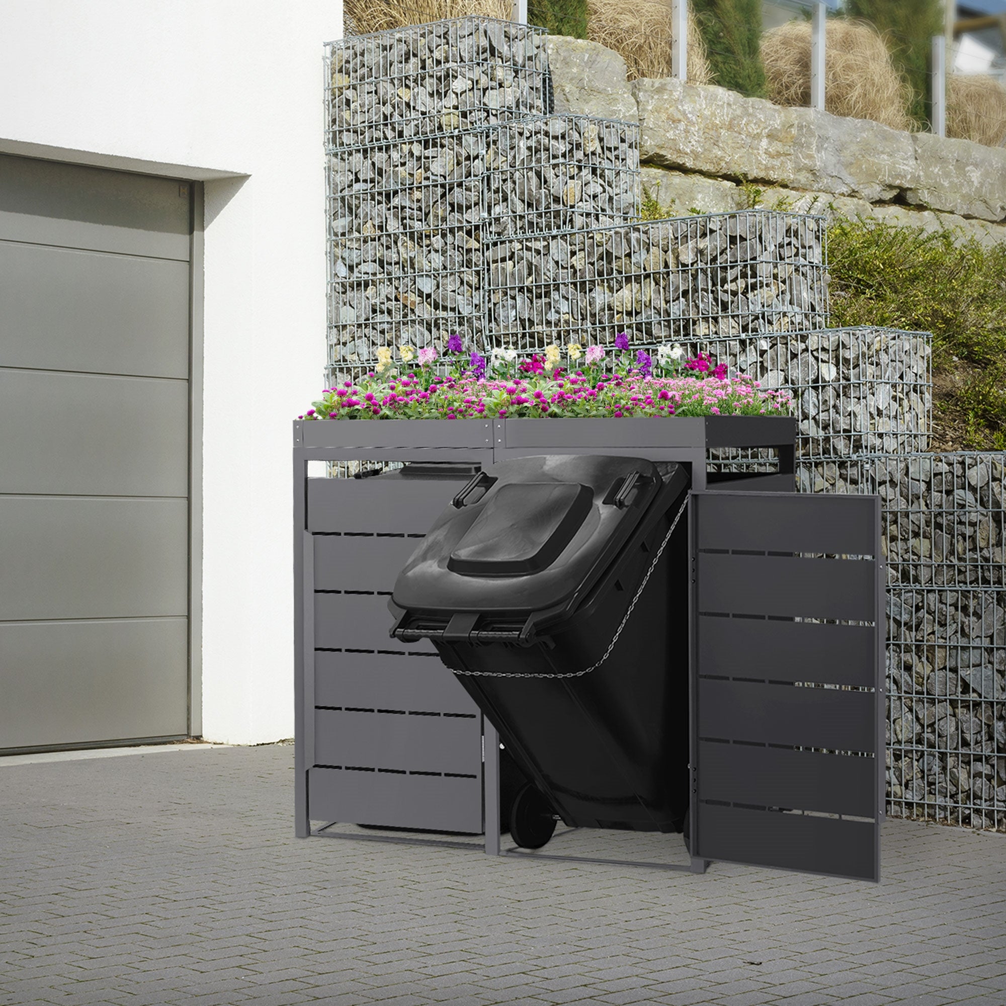 Mülltonnenbox mit geöffneter Tür, Mülltonne sichtbar, vor einer Steinmauer.