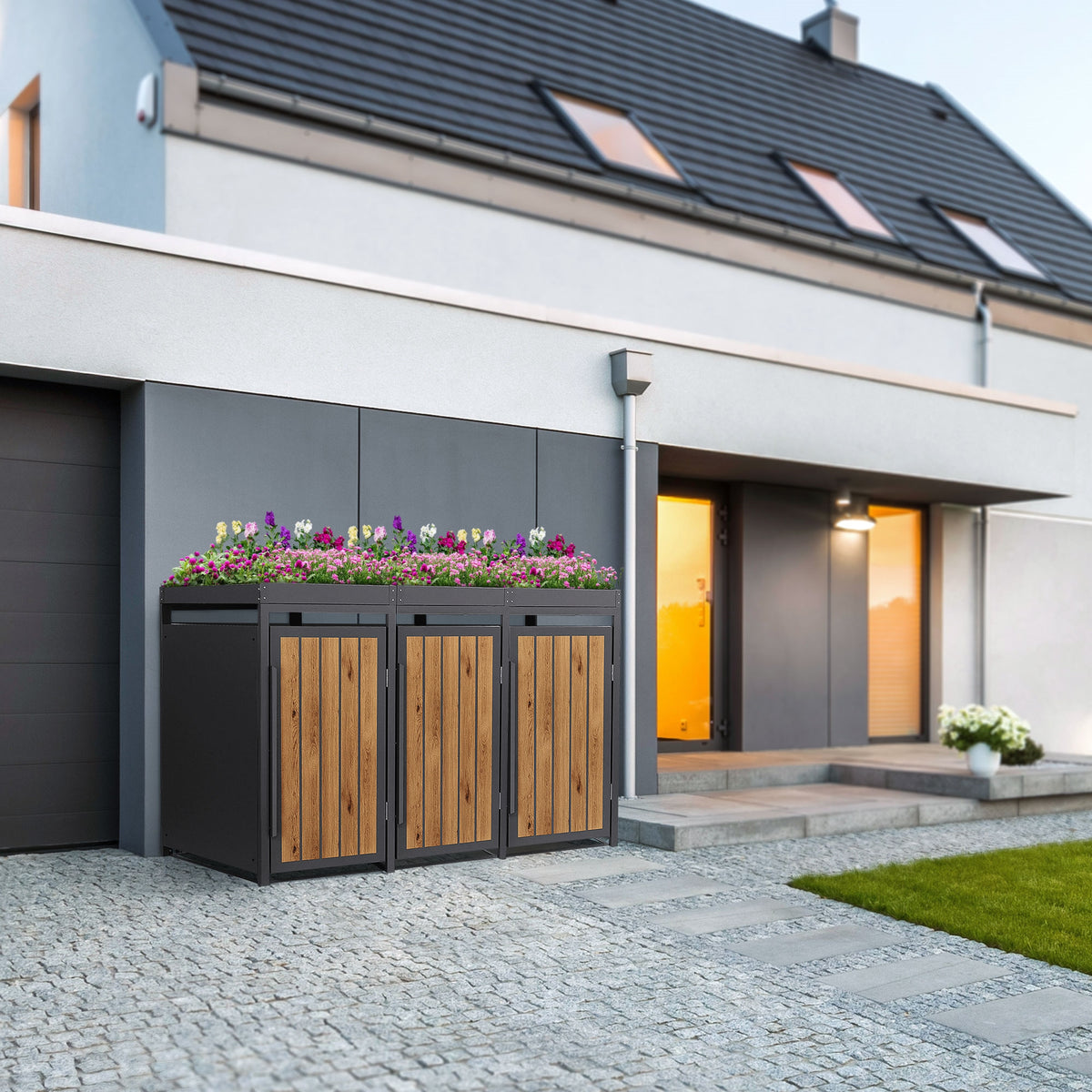 Drei Mülltonnenboxen aus Holz und Metall vor einem modernen Haus mit Blumen.