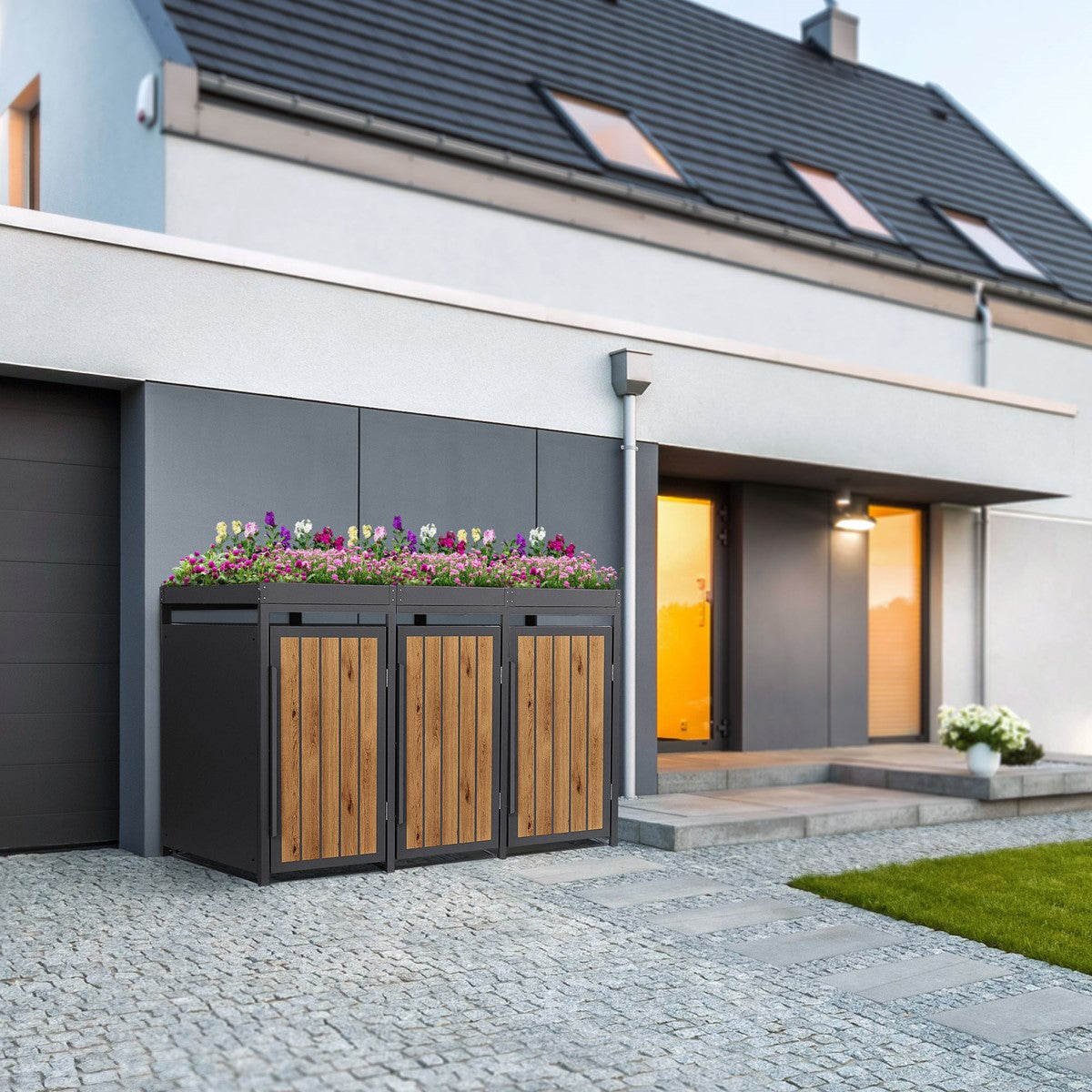 Drei Mülltonnenboxen aus Holz und Metall vor einem modernen Haus mit Blumen.