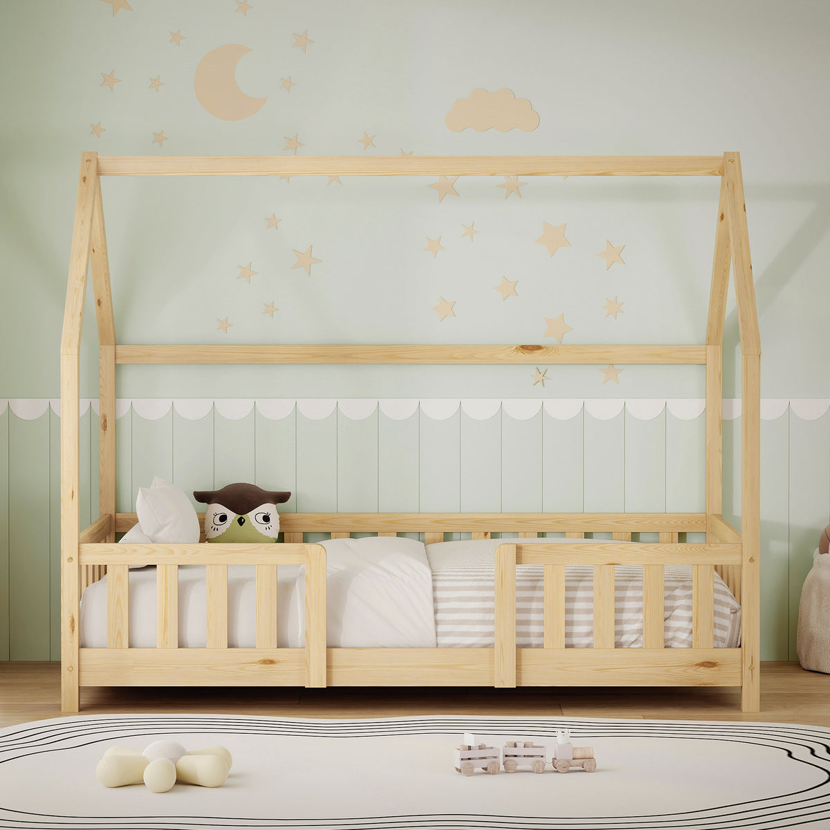 Lit en bois avec forme de toit, coussin et jouets sur le matelas, mur avec lune et étoiles.