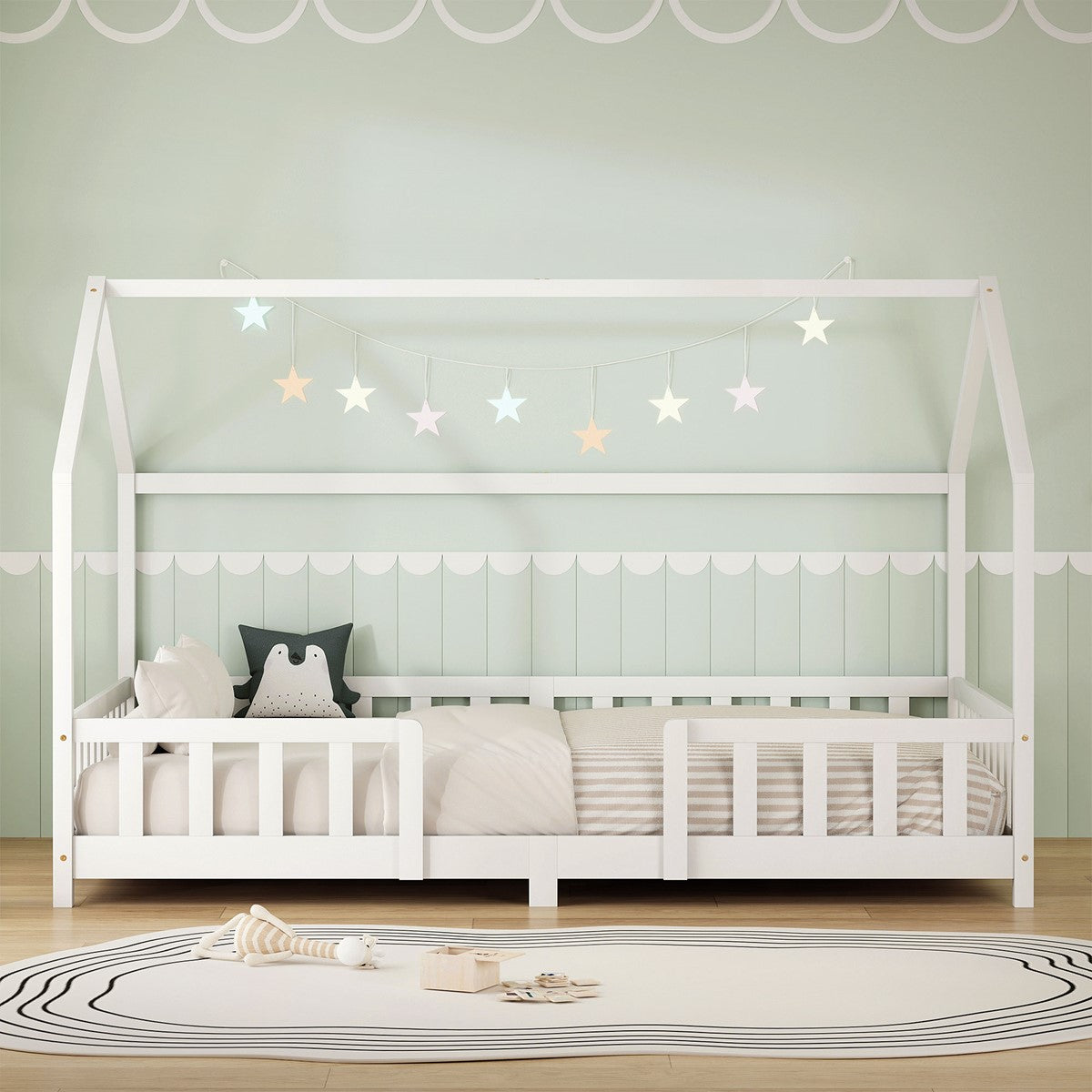 Weißes Kinderbett im Hausdesign, mit Kissen und Sternenlichtern, auf grünem Hintergrund.