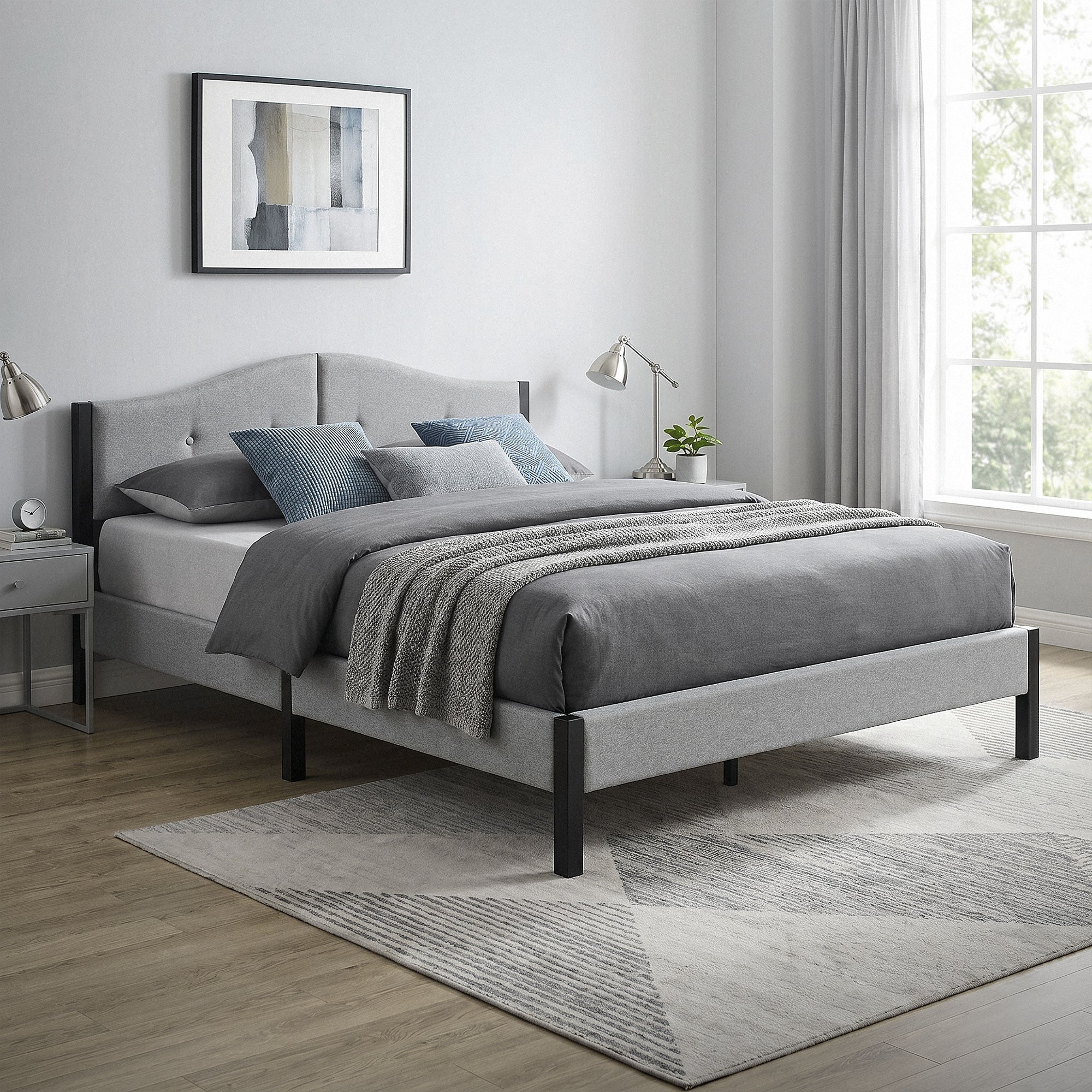 Bett mit grauem Bezug, Kissen und Tagesdecke, Fenster mit Vorhängen im Hintergrund.