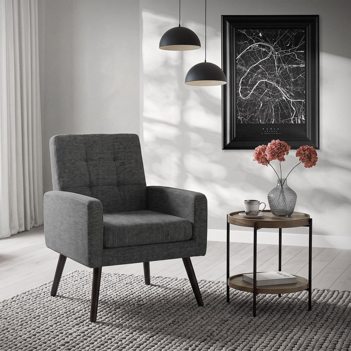 Poltrona cinzenta-escura com estofamento quadrado, mesa e flores ao fundo.