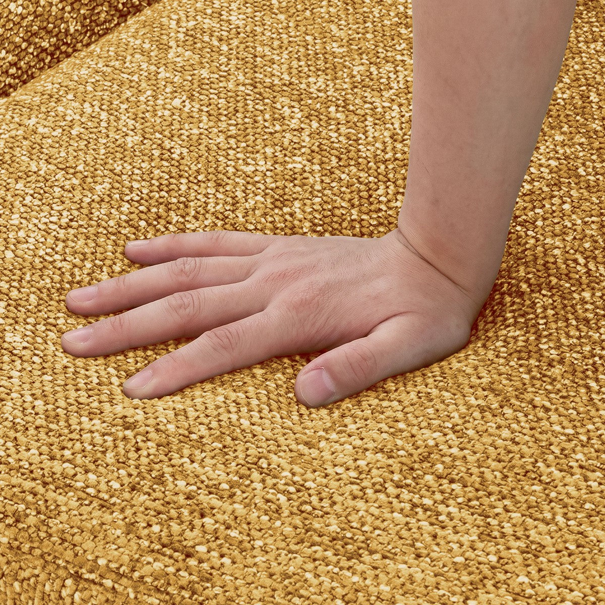 Eine Hand drückt auf einen goldbraunen, grob gewebten Teppich.