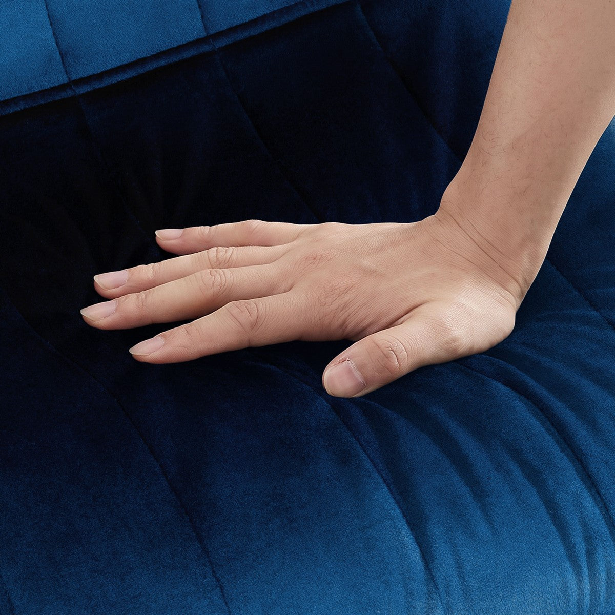 Una mano presiona el asiento azul oscuro de una silla, con pespuntes longitudinales.