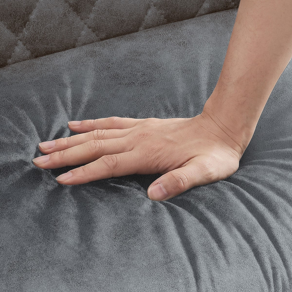 Eine Hand drückt in eine graue, gepolsterte Sitzfläche und erzeugt sichtbare Falten im Stoff.