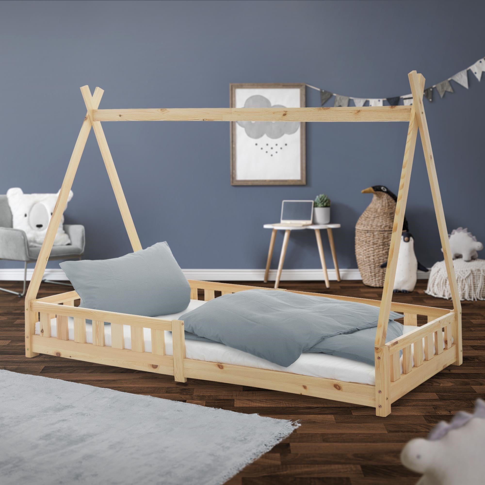 Ein Holz-Kinderbett in Naturfarbe mit Kissen und Decke im Raum.