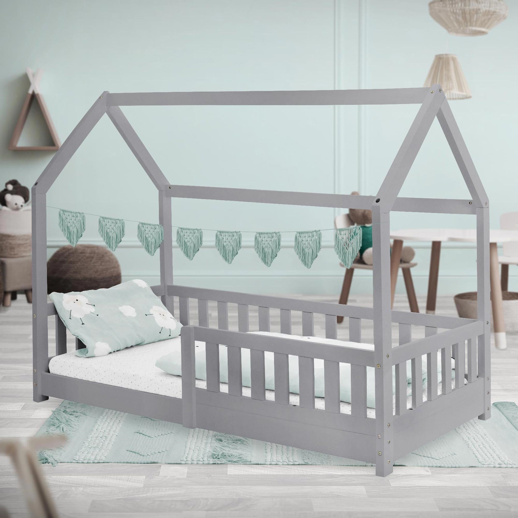 Cama con techo de casa en una habitación, decorada con cojines y guirnalda.