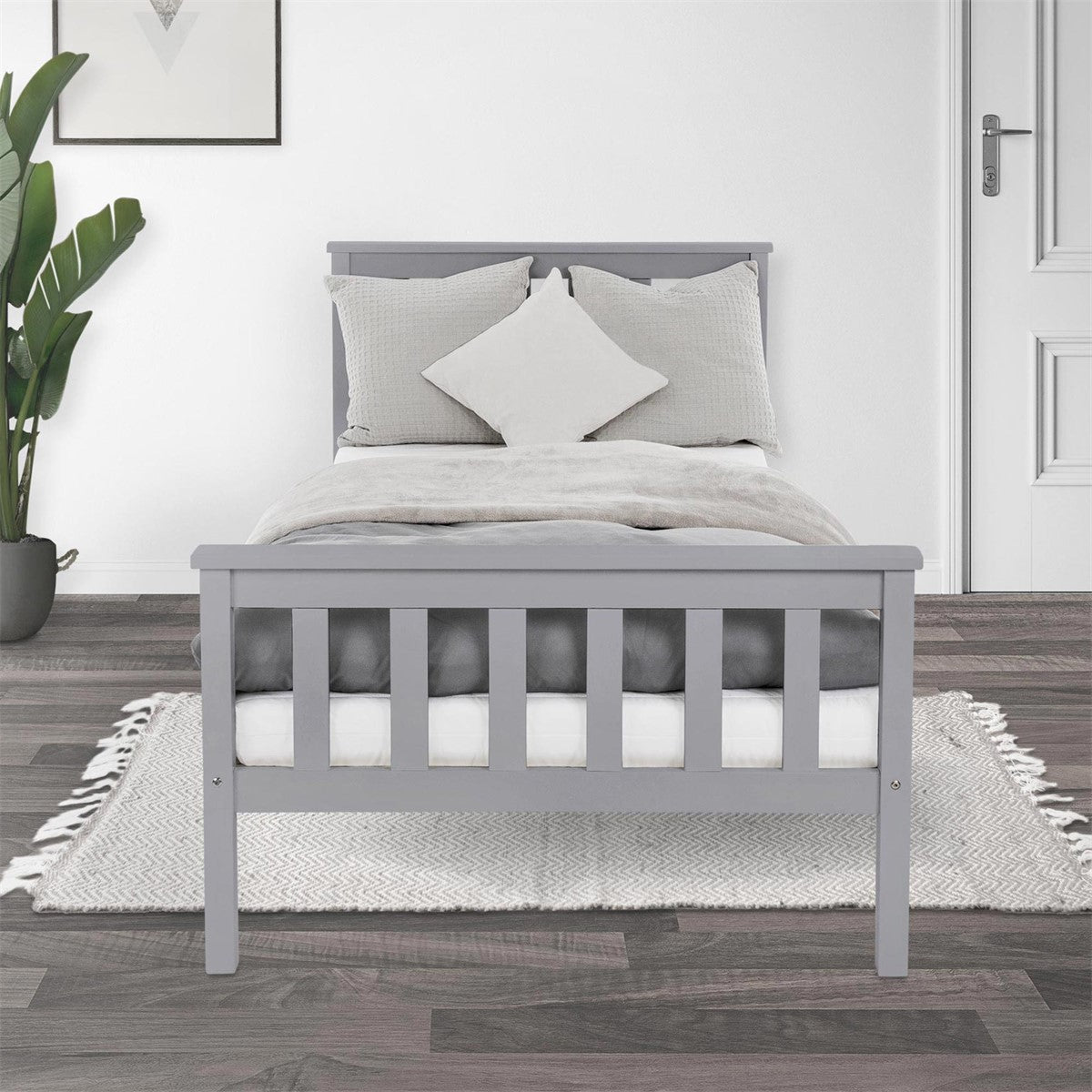 Graues Bett mit Kissen und Decke, auf einem Holzboden.