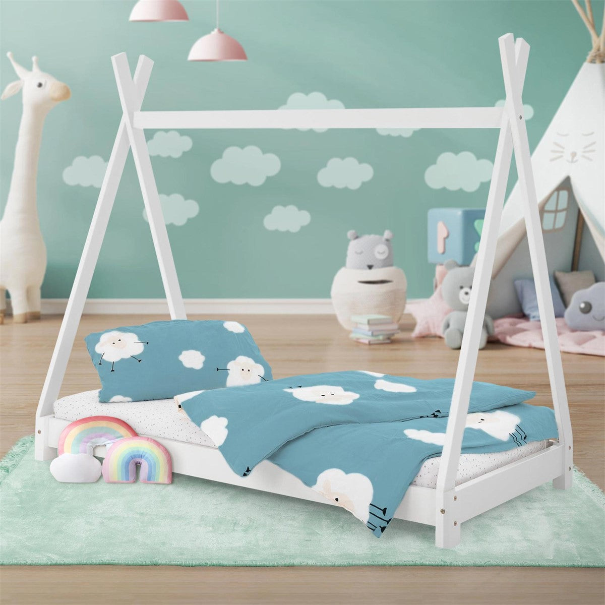 Un lit d’enfant de style tente avec du linge de lit à motifs de nuages et des jouets arc-en-ciel.