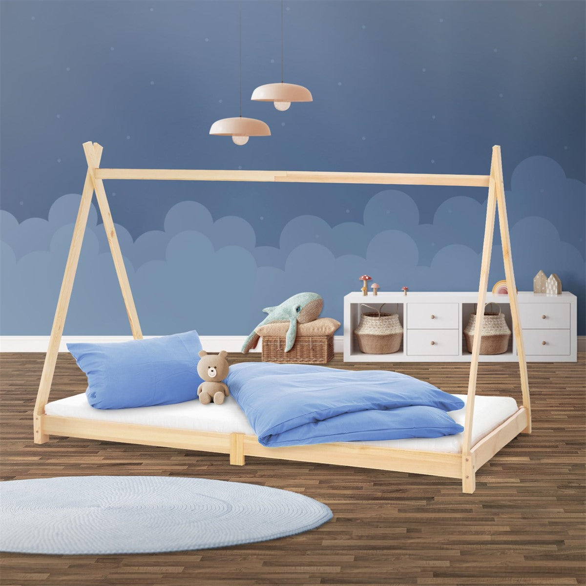 Bed in de kinderkamer met blauwe kussens en deken, houten frame en muur met wolkenpatroon.