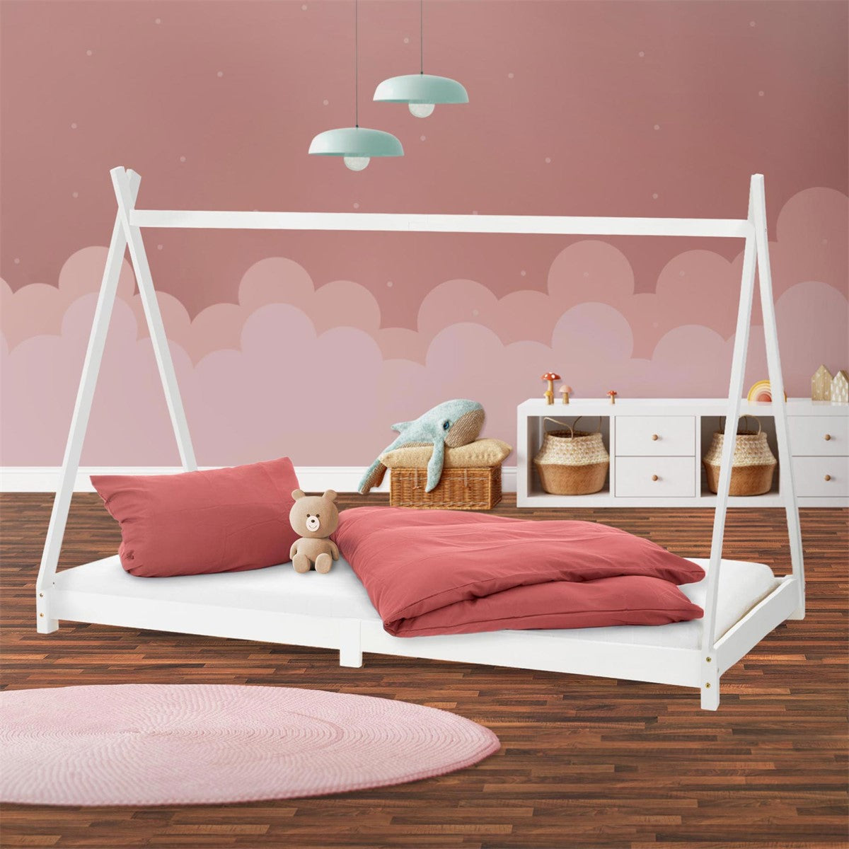 A white child's bed with a pillow and blanket, a teddy bear, and a pink background.