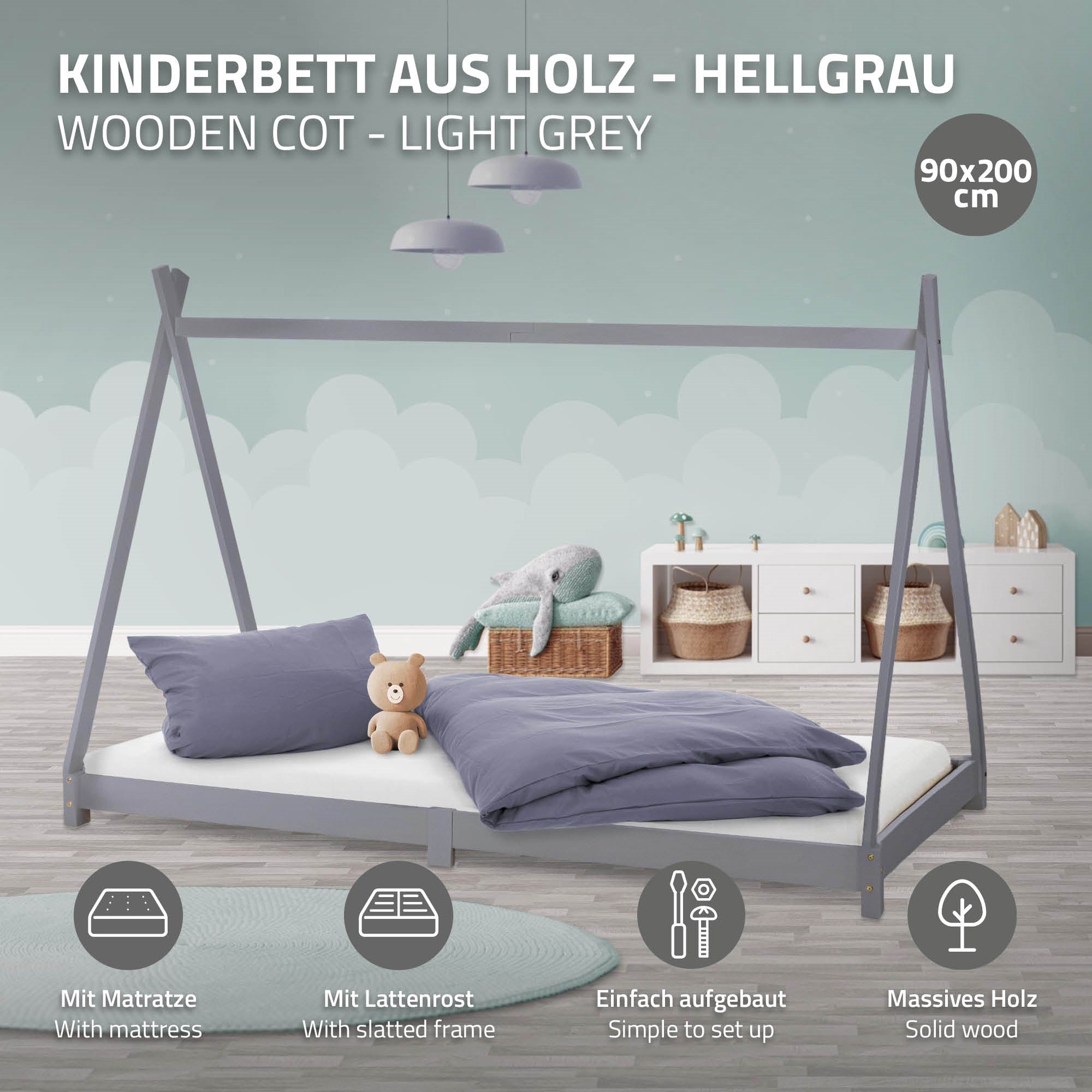 Ein hellgraues Kinderbett mit Kissen, Decke und einem Teddy, vor einem hellen Raum.