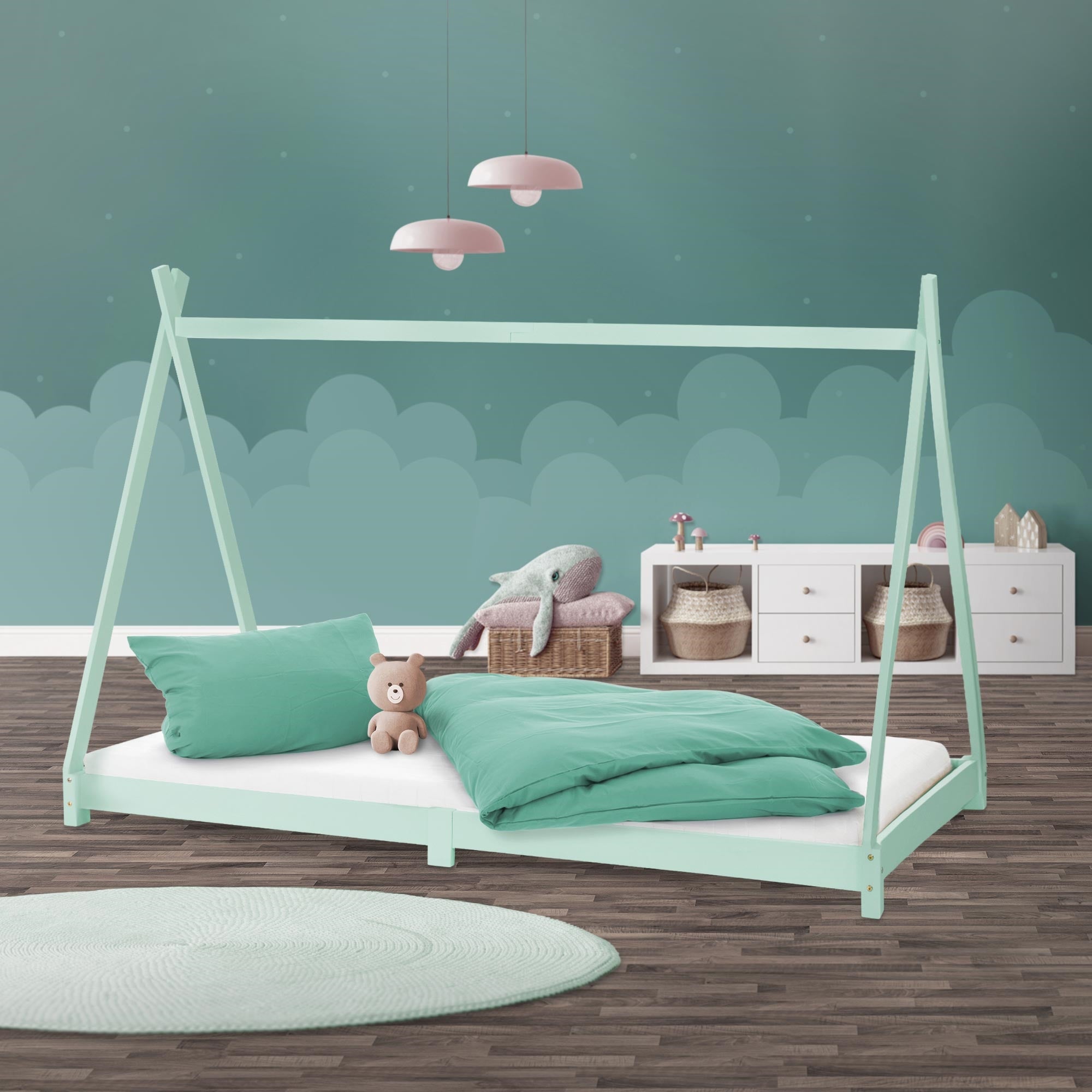 Mintgrünes Bettgestell mit Kissen, Decke und einem Teddybär auf einer Matratze.