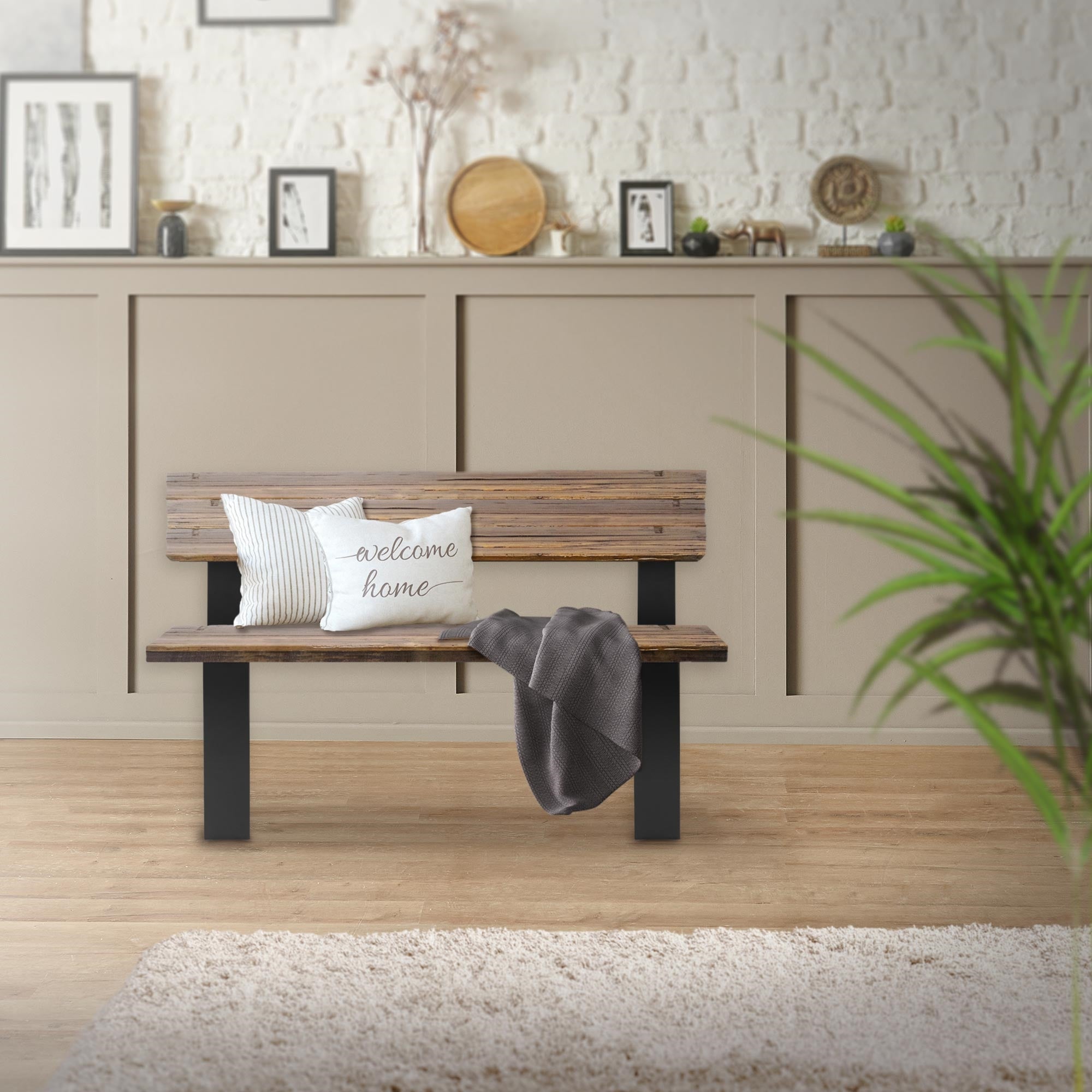 Holzbank mit Kissen und Decke, vor einer hellen Wand mit Bildern.