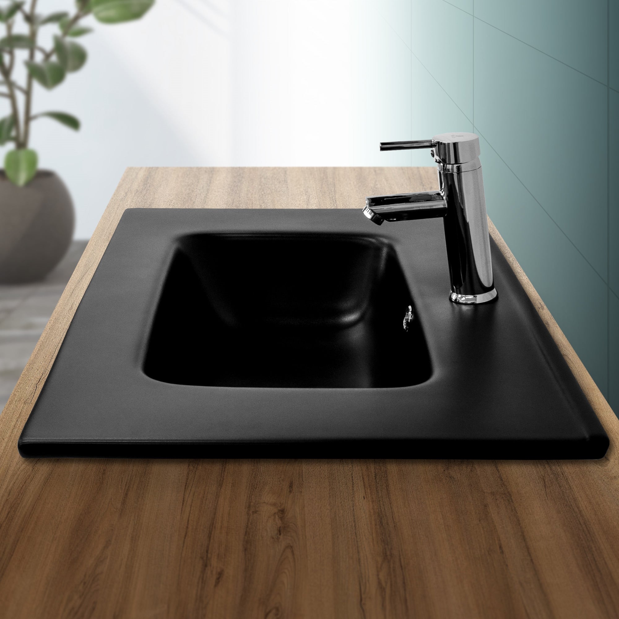 Schwarzes Waschbecken auf Holzplatte mit Wasserhahn und Pflanze im Hintergrund.