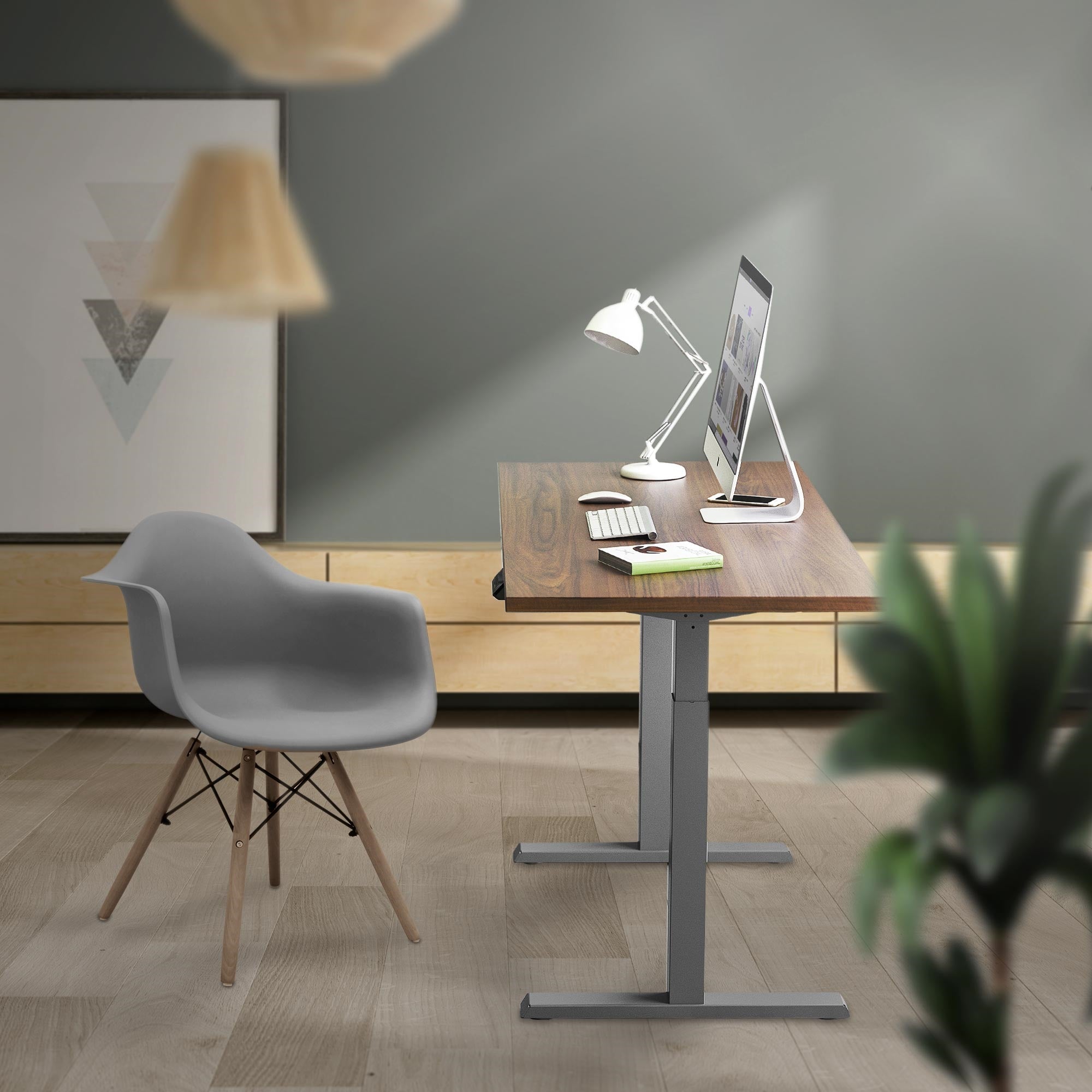 Ein moderner Schreibtisch mit Computer, Lampe und Stuhl in einem Raum mit grauen Wänden.