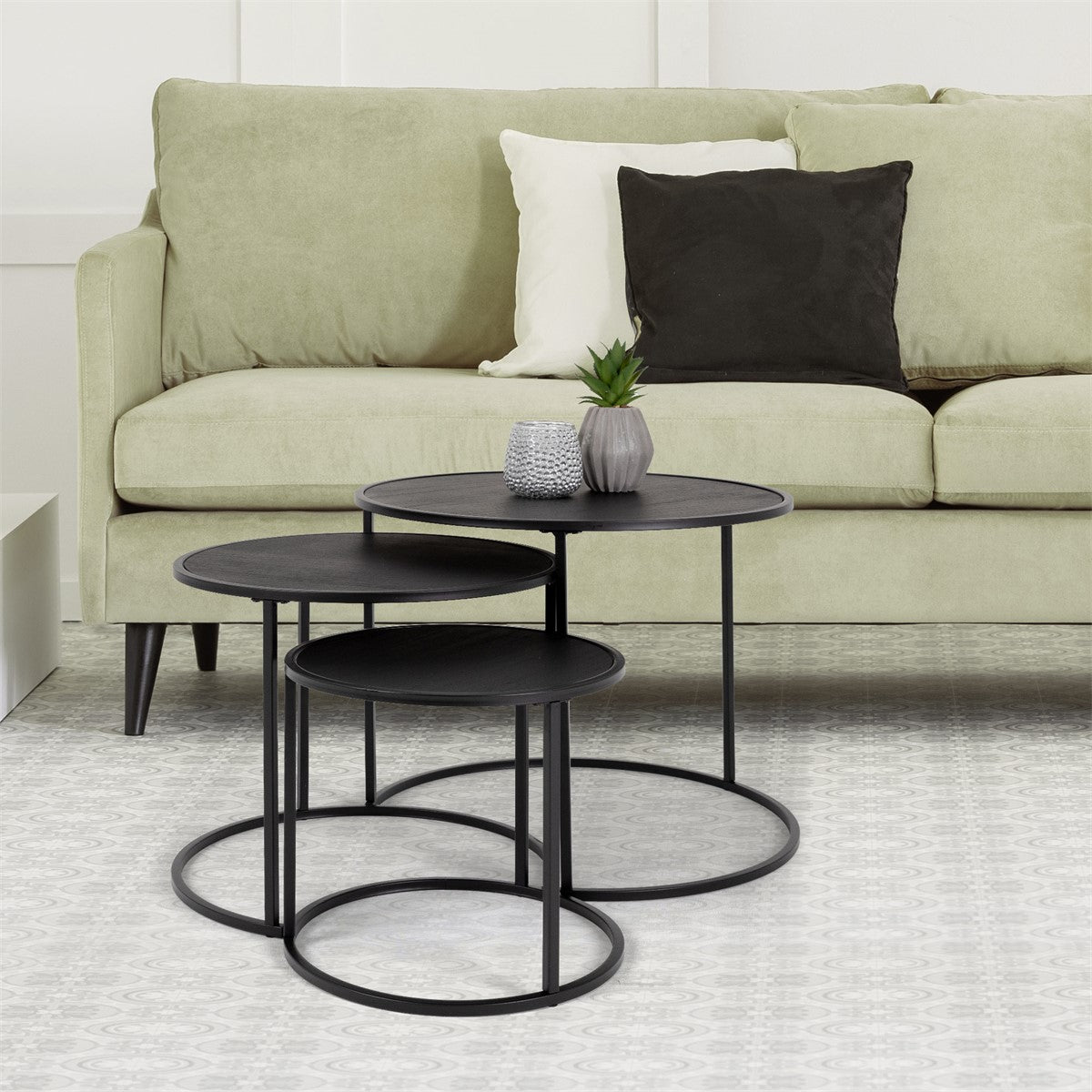 Trois tables d’appoint noires devant un canapé vert.