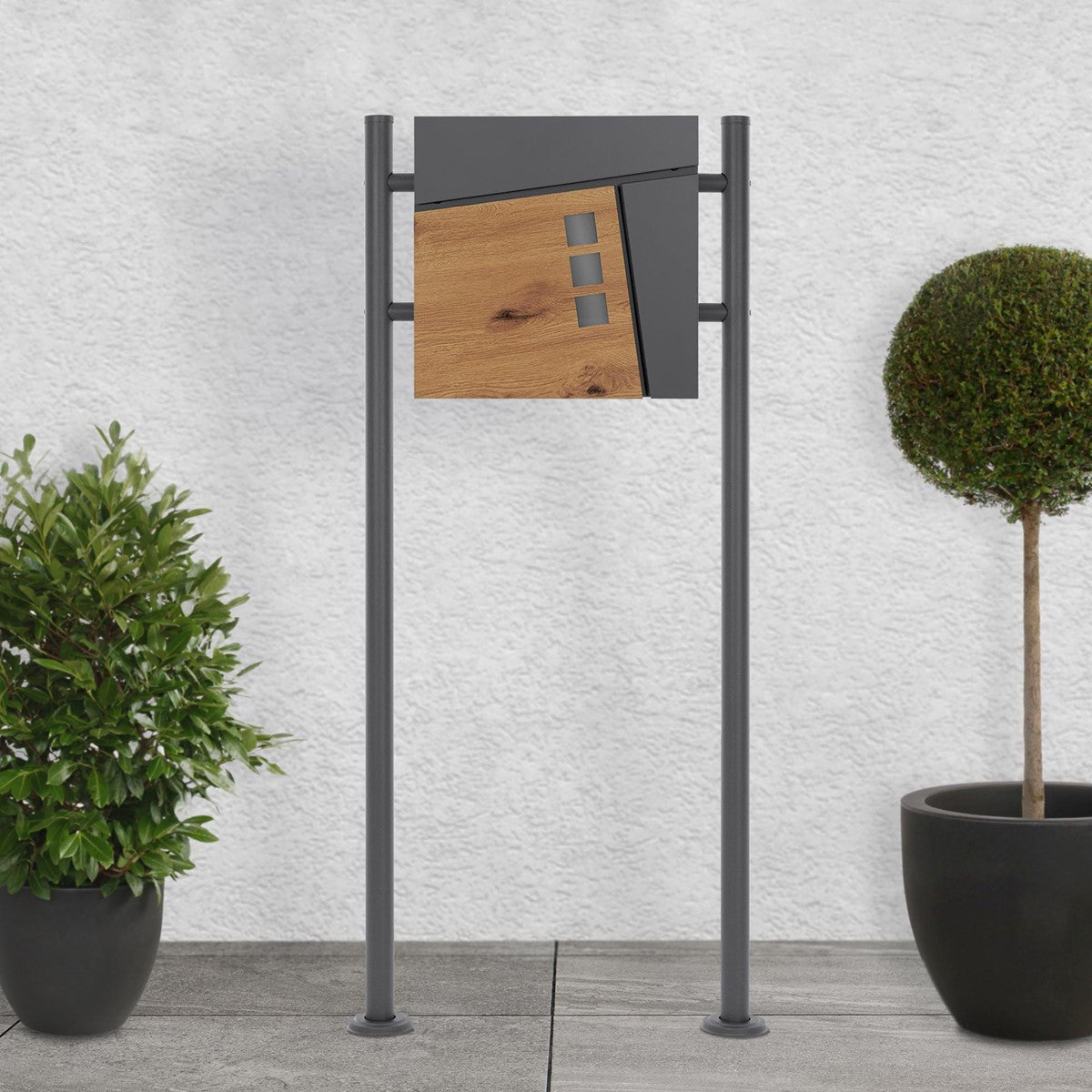 Mailbox with a wooden front on a sturdy stand, next to plants.