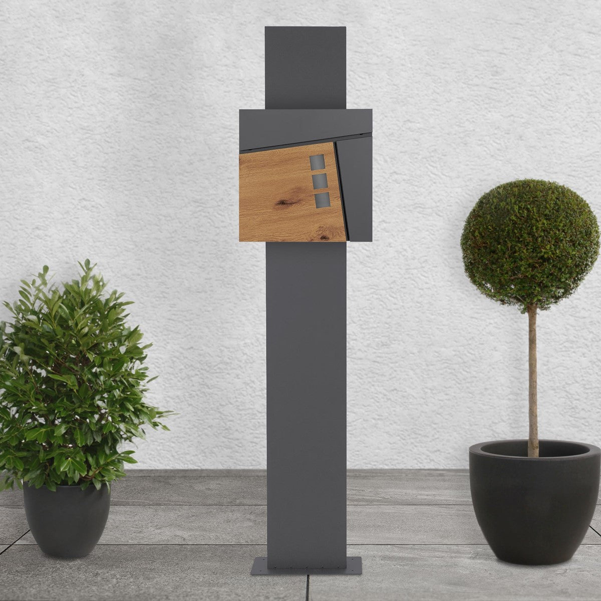 Mailbox on a stand with a wooden front, surrounded by plants.