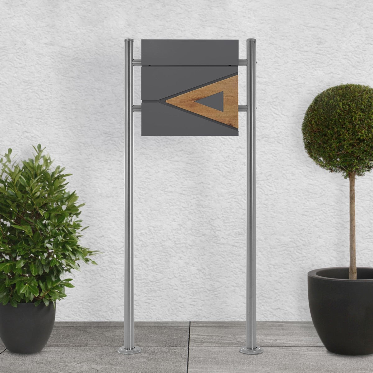 Mailbox with a wooden element on a pavement between two plants.