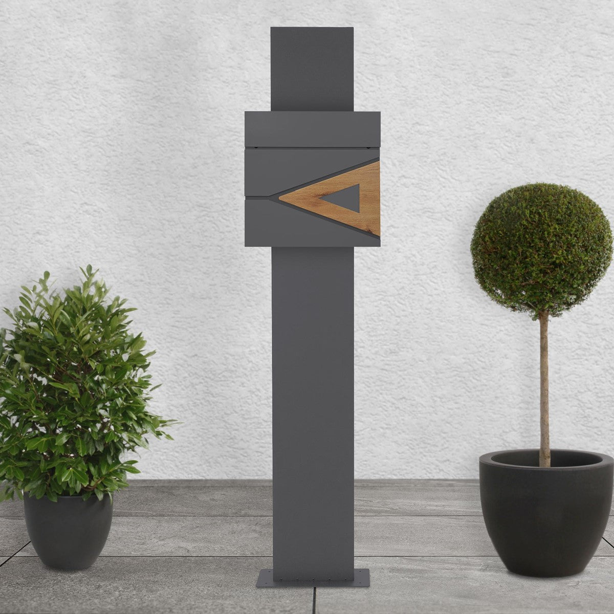 Modern letterbox on a tall stand, surrounded by plants.