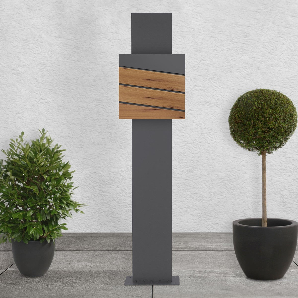 Grey pillar with wooden panels, surrounded by two round plants in pots.