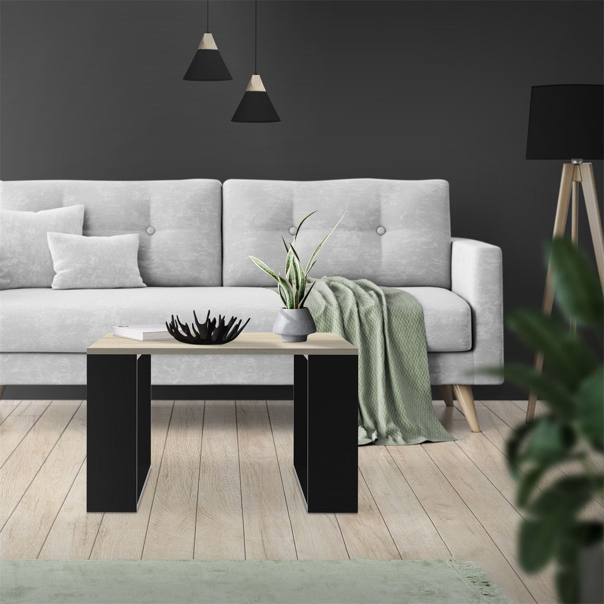 Helles Wohnzimmer mit grauem Sofa, Tisch und Pflanzen auf dem Boden.
