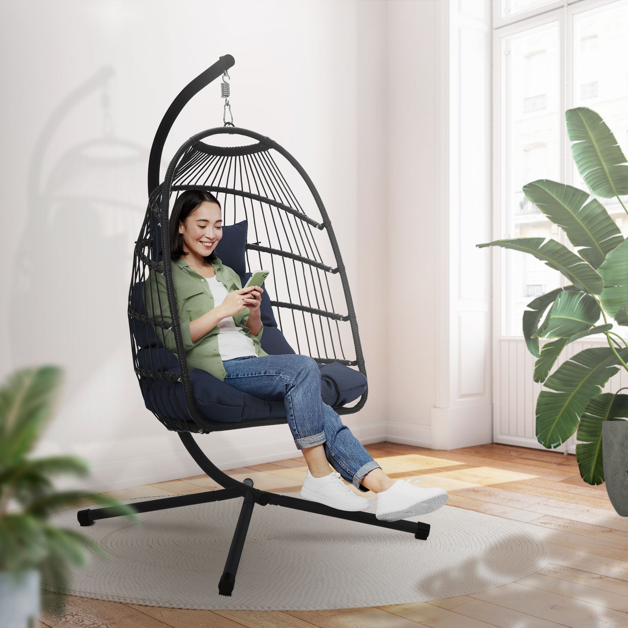 Vrouw zit in een hangstoel en gebruikt een smartphone in een lichte kamer.