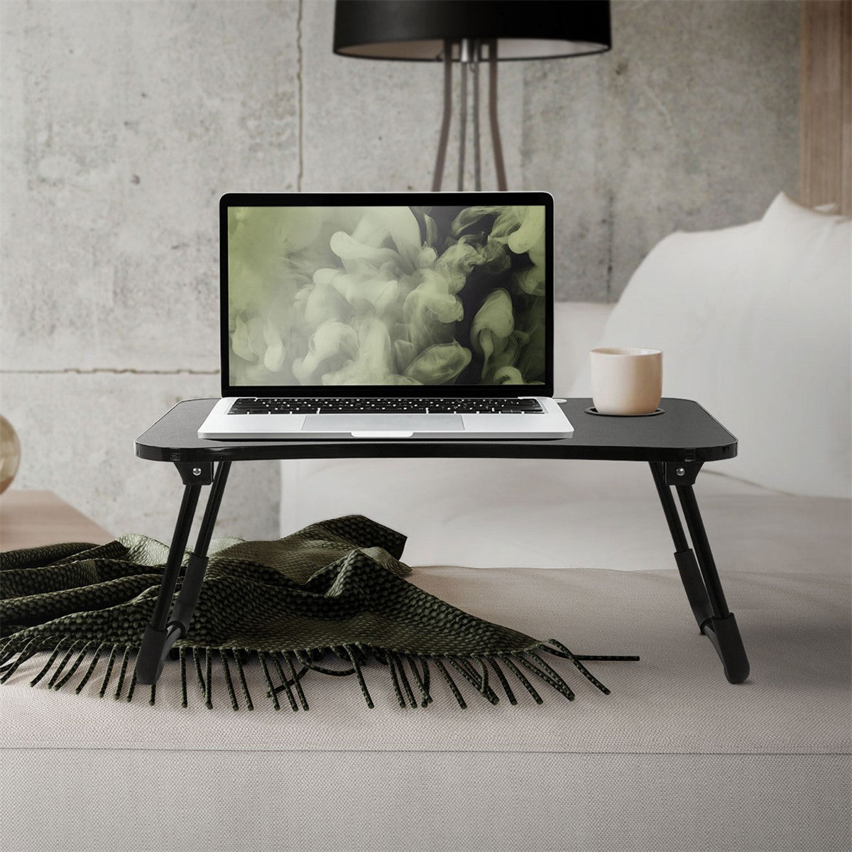 A laptop on a folding table with a cup beside it and a blanket.