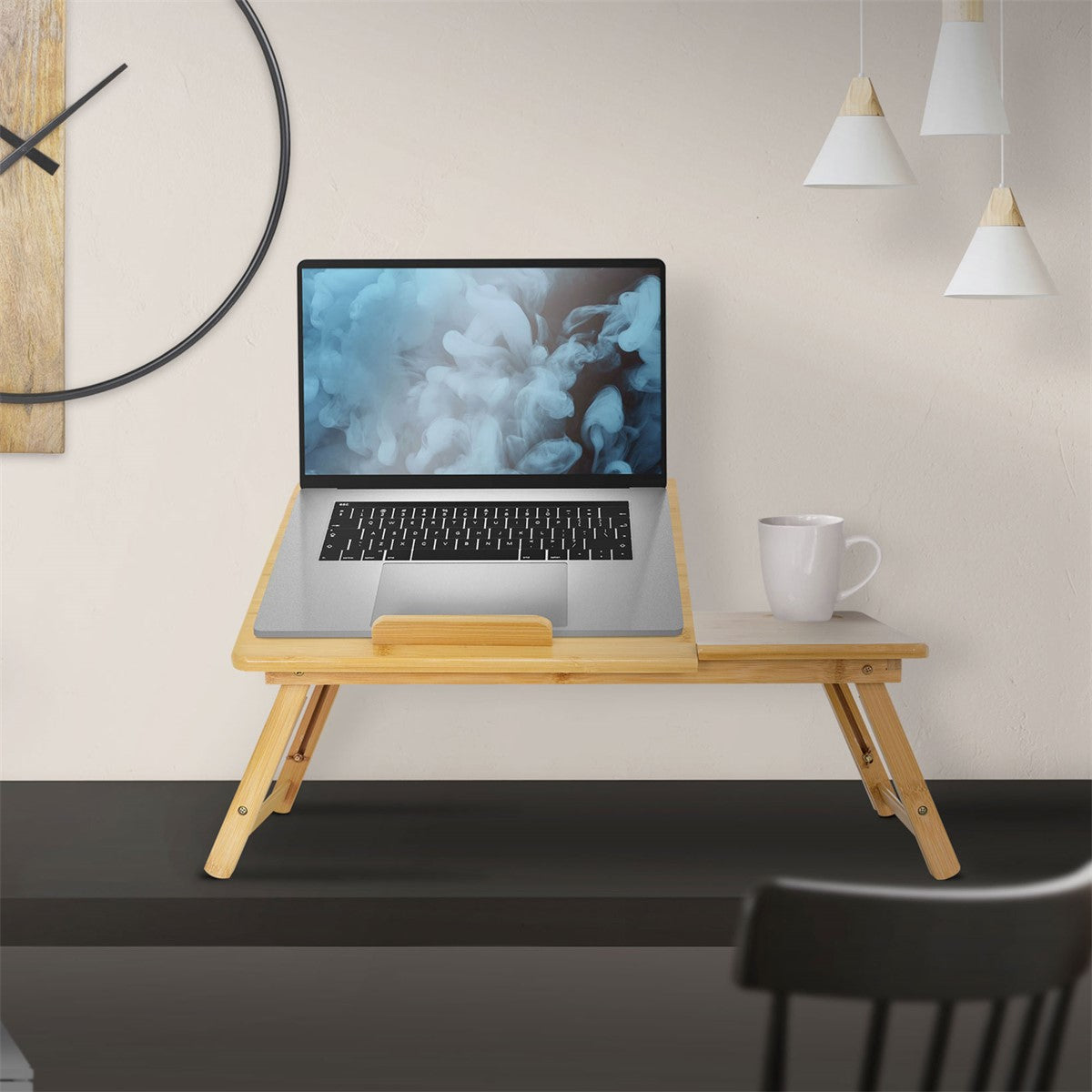 A folding bamboo table with a laptop and a cup.