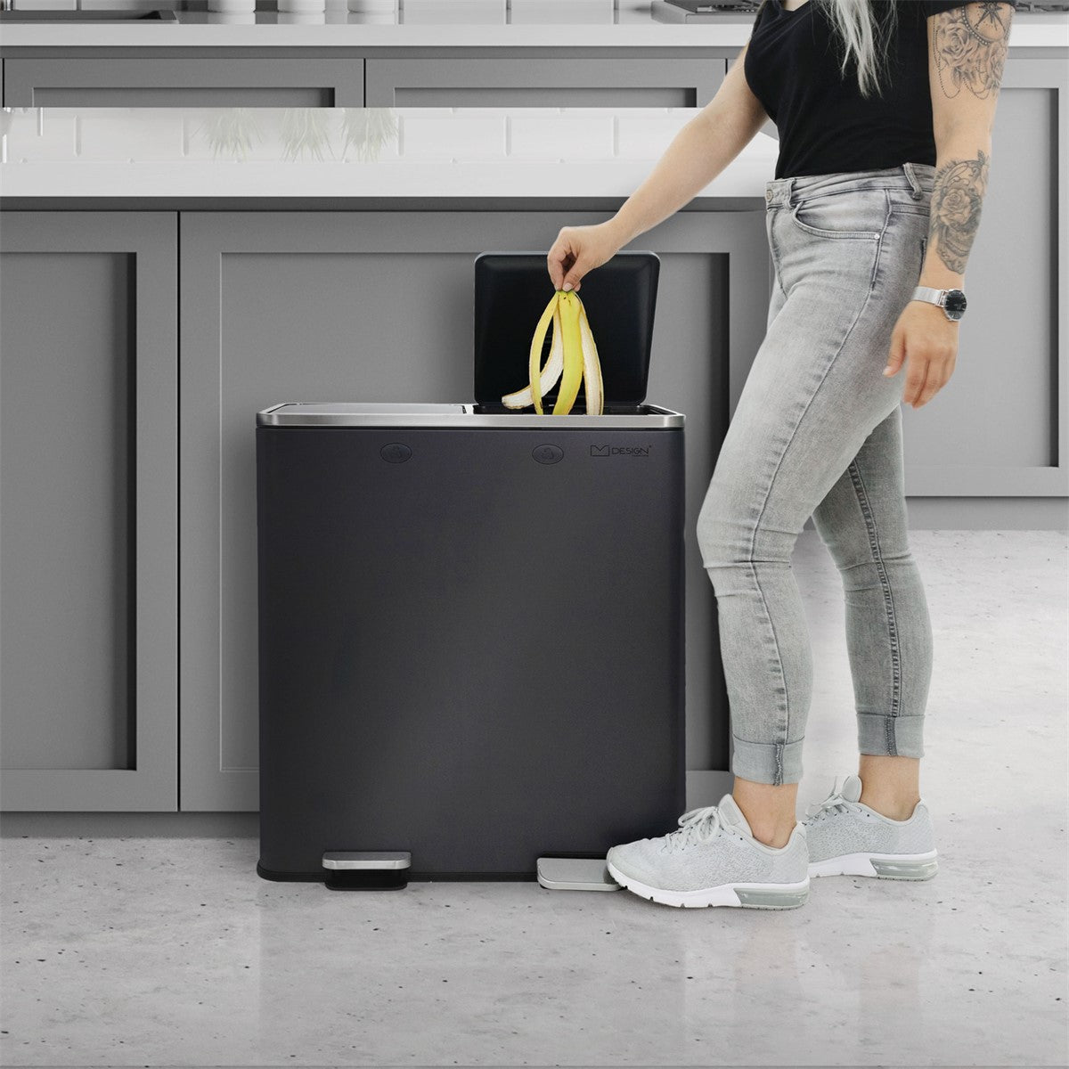 Person mit langen Haaren wirft eine Banane in einen Müllbehälter.