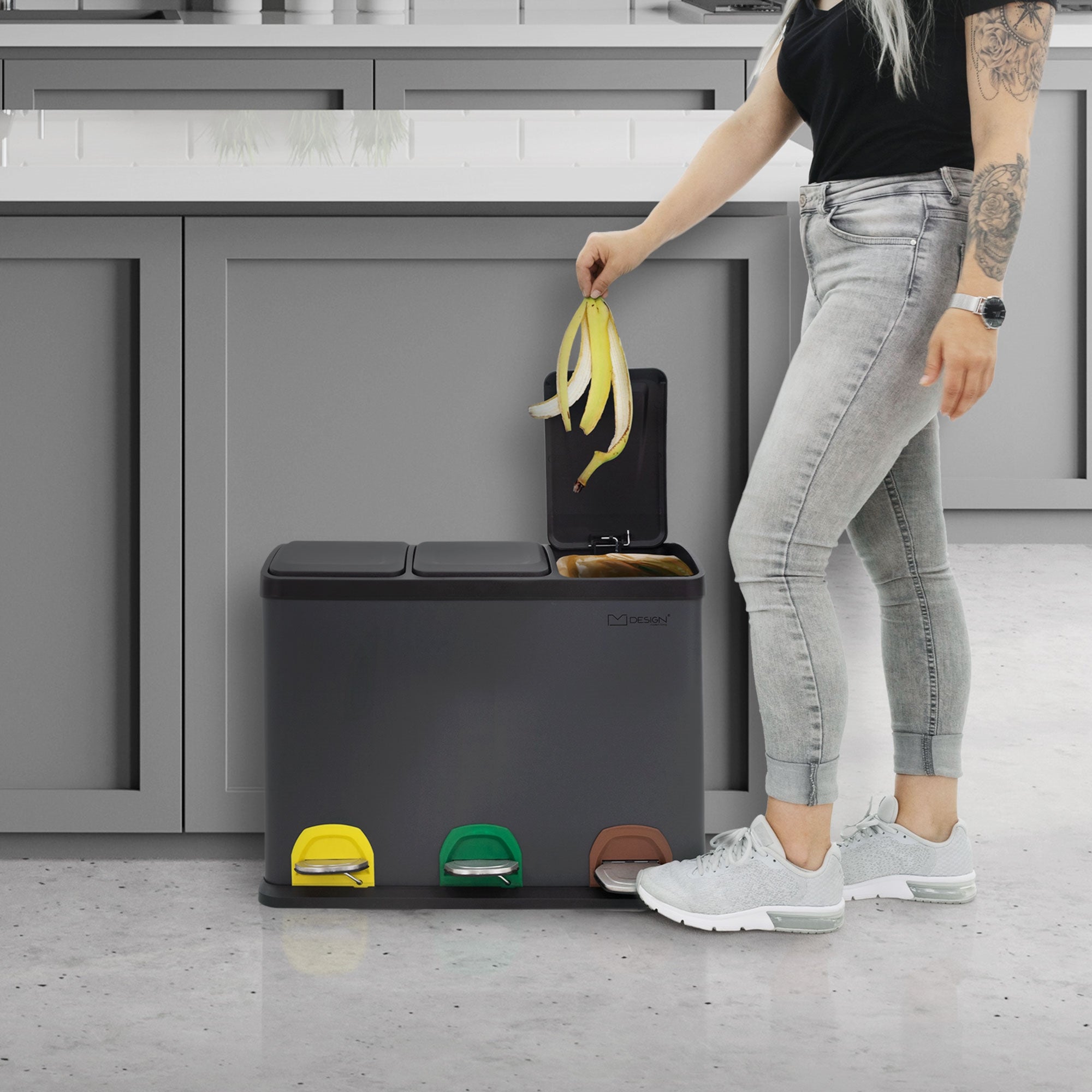 Person mit langen Haaren steht neben einem Mülltrennsystem und wirft eine Banane hinein.