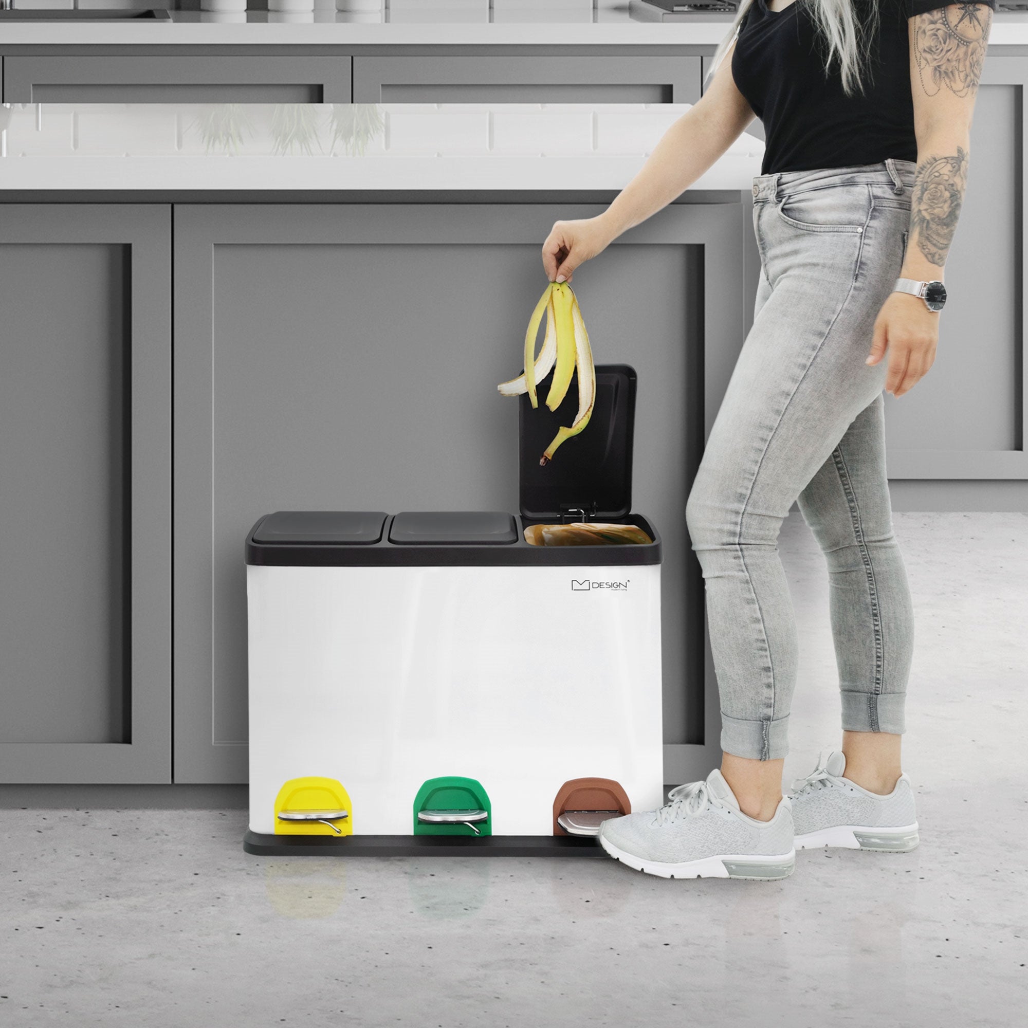 Person mit langen Haaren, die eine Banane in einen Mülltrennungsbehälter wirft.