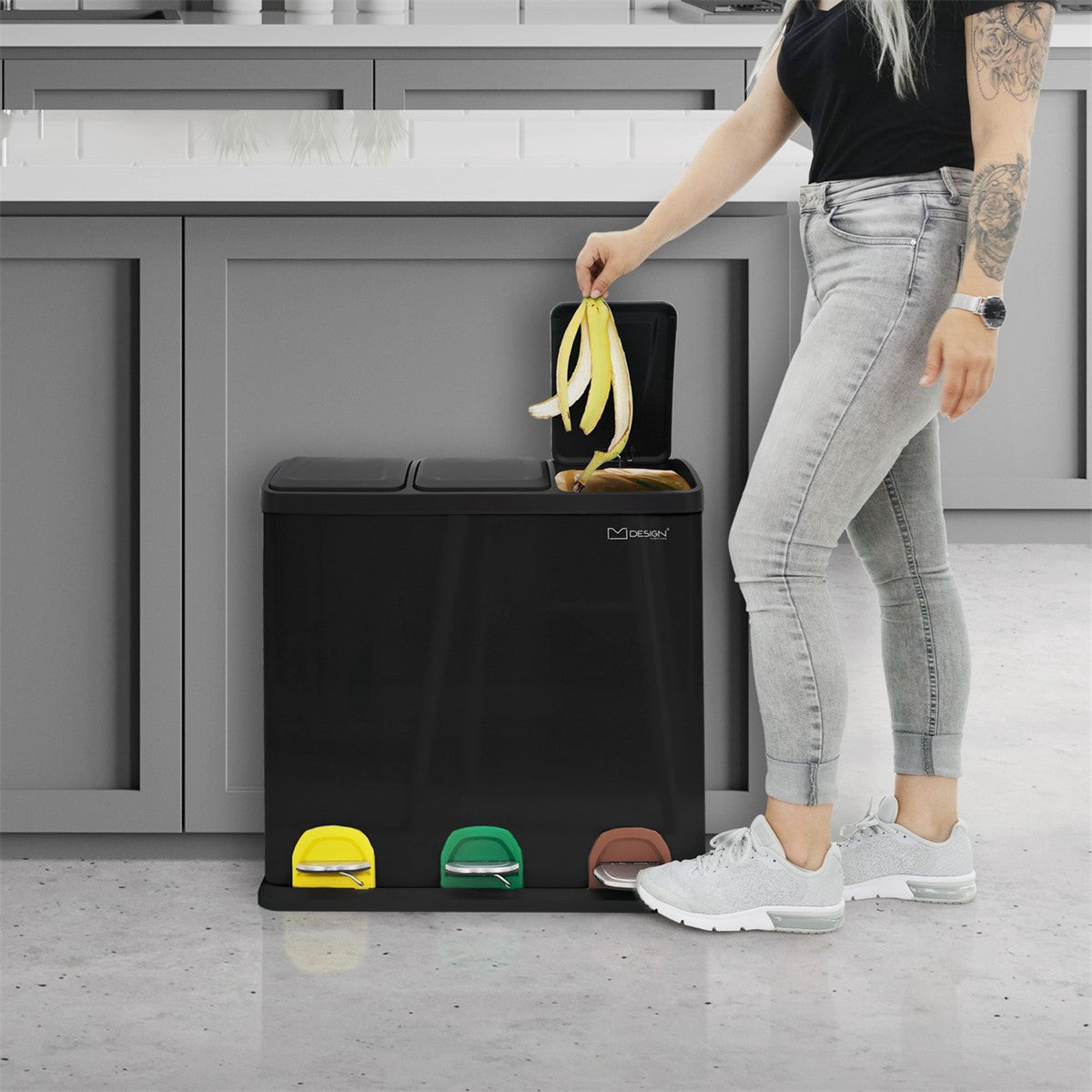 Person mit langen Haaren, die eine Banane in einen Mülleimer mit drei Fächern wirft.
