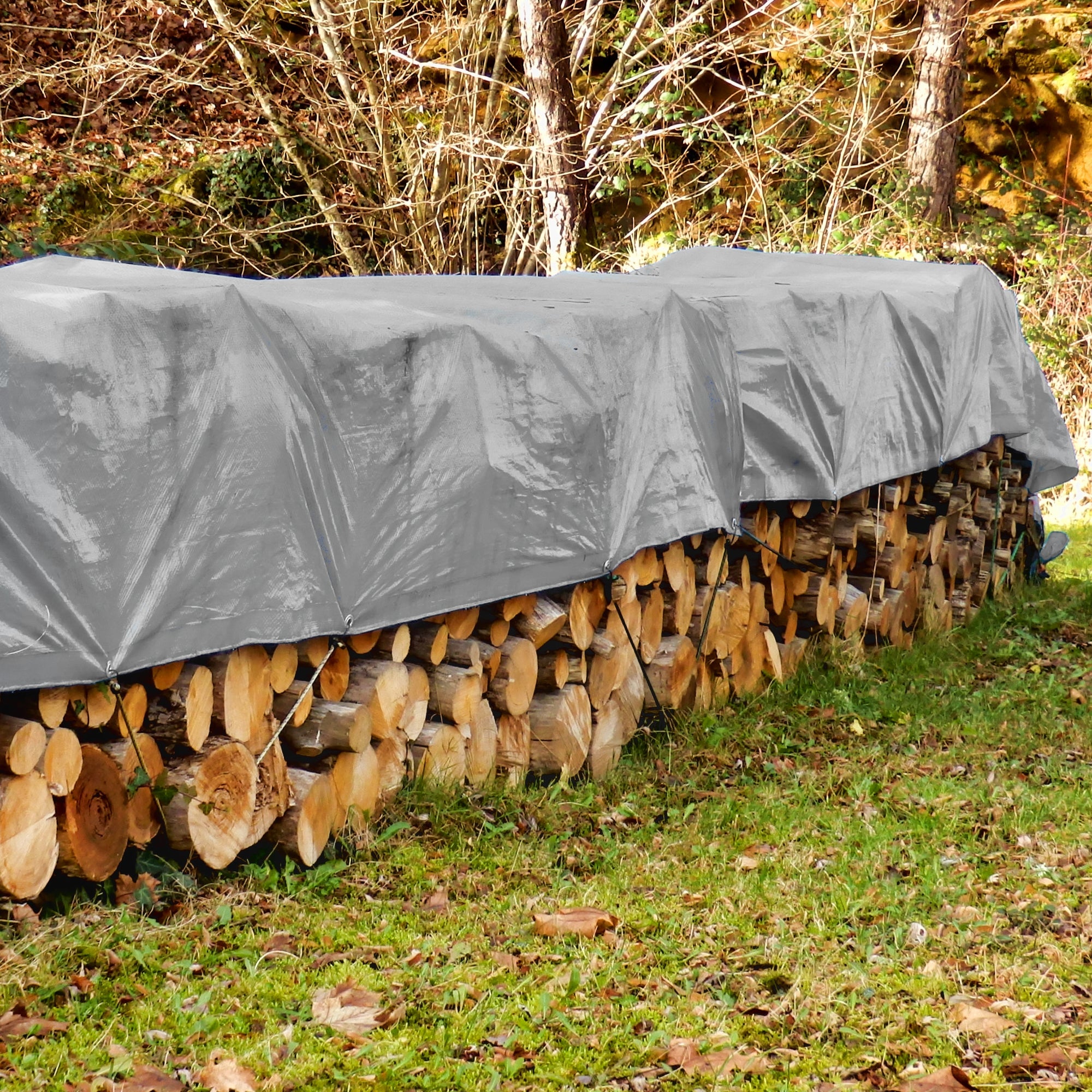 Telo grigio che protegge i tronchi di legno dalla pioggia, all'aperto.