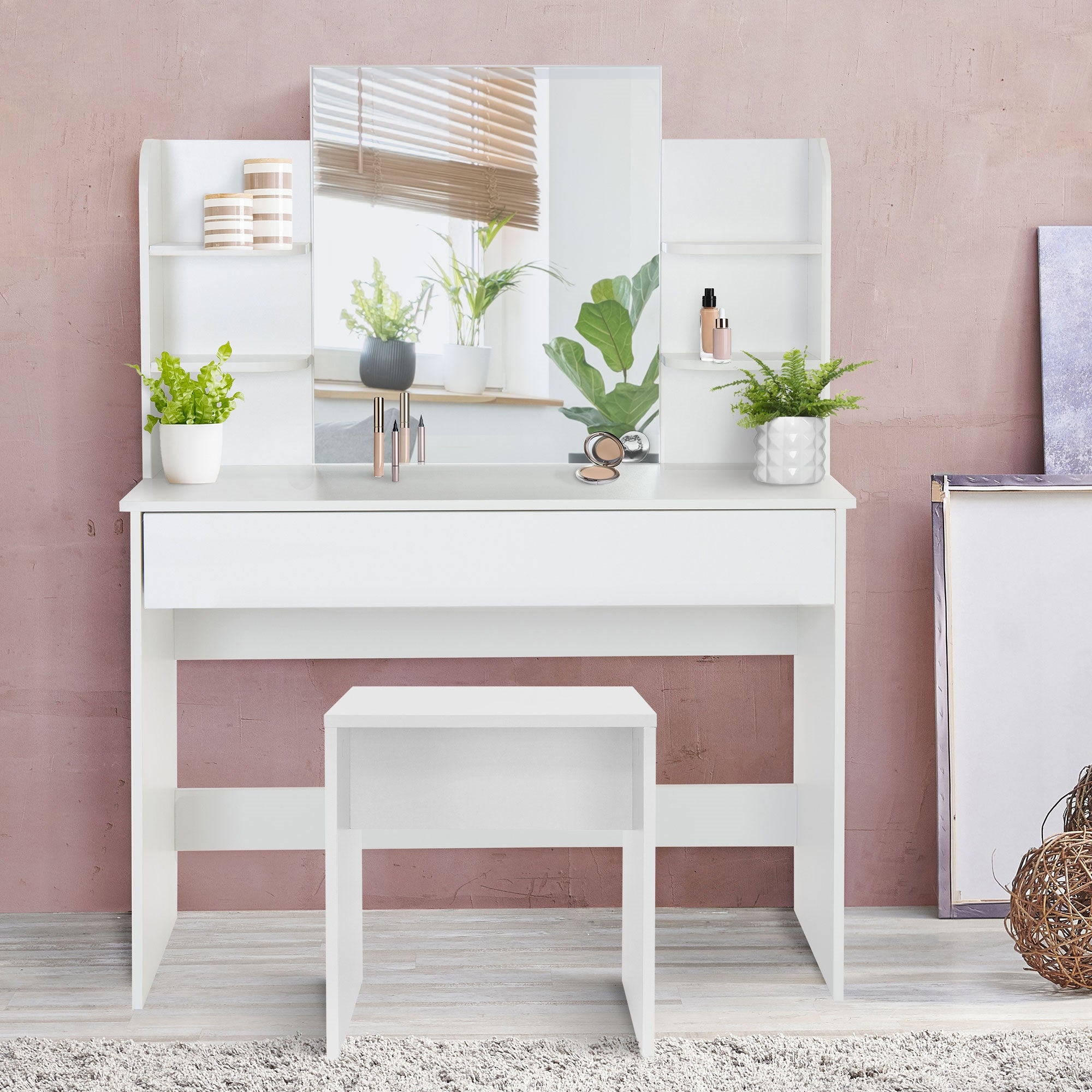 Ein weißer Schminktisch mit Pflanzen, Spiegel und Hocker vor einer rosa Wand.
