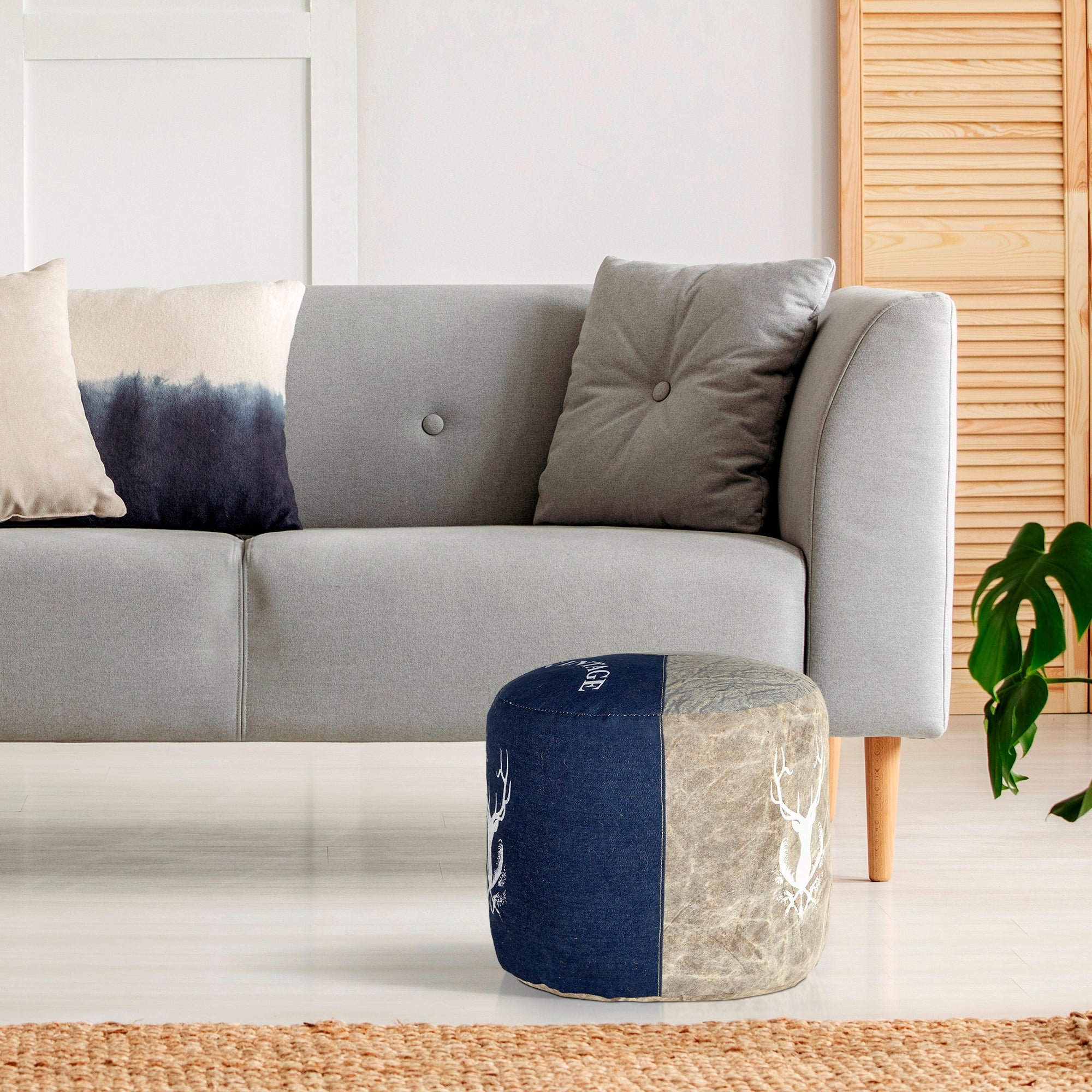 En rund pouf lavet af jeansstof ved siden af en grå sofa med puder.