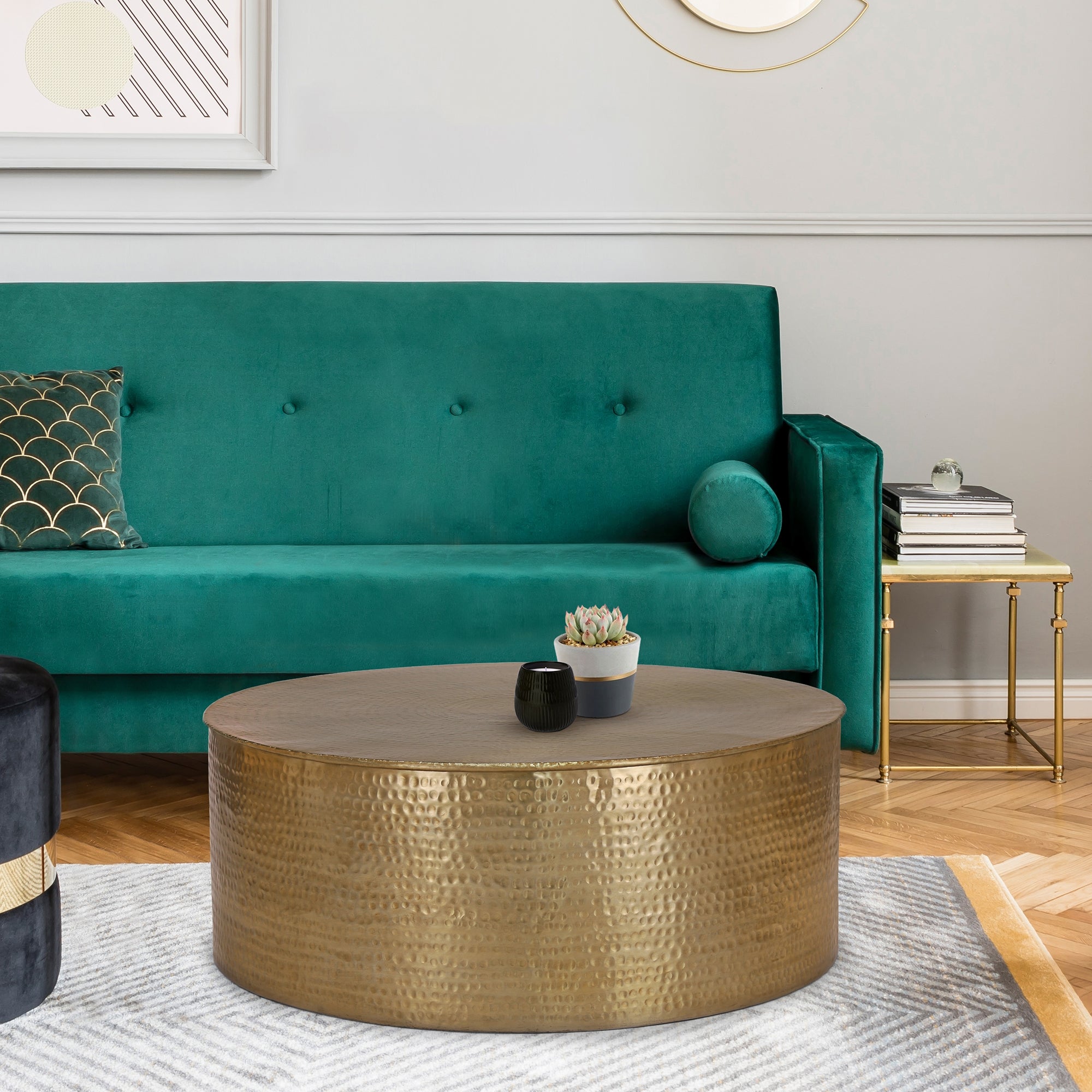 Grünes Sofa mit Kissen und runder, goldfarbener Tisch auf einem Teppich.