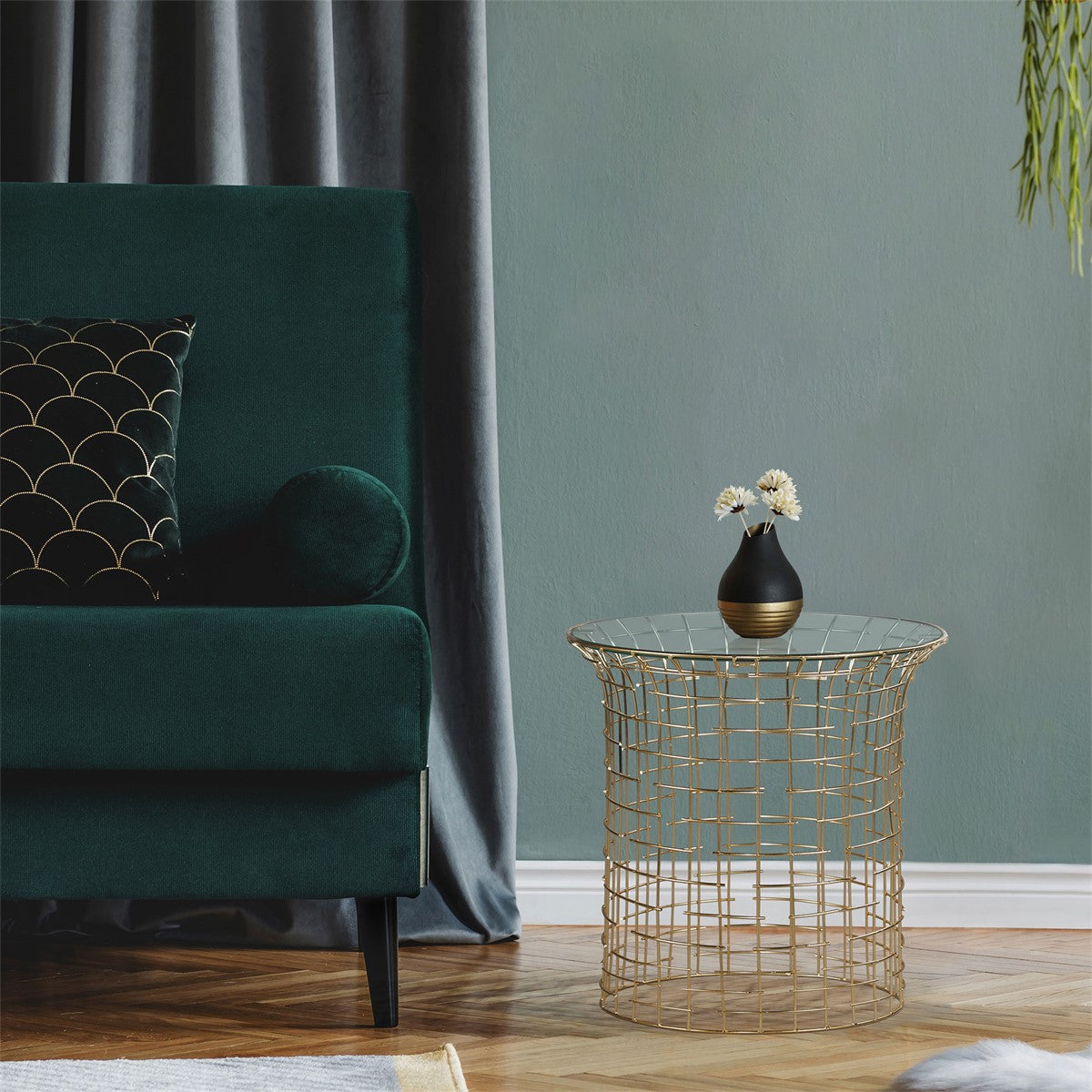 Grüner Sofa mit Kissen, daneben ein goldener Beistelltisch mit schwarzem Vase und Blumen.