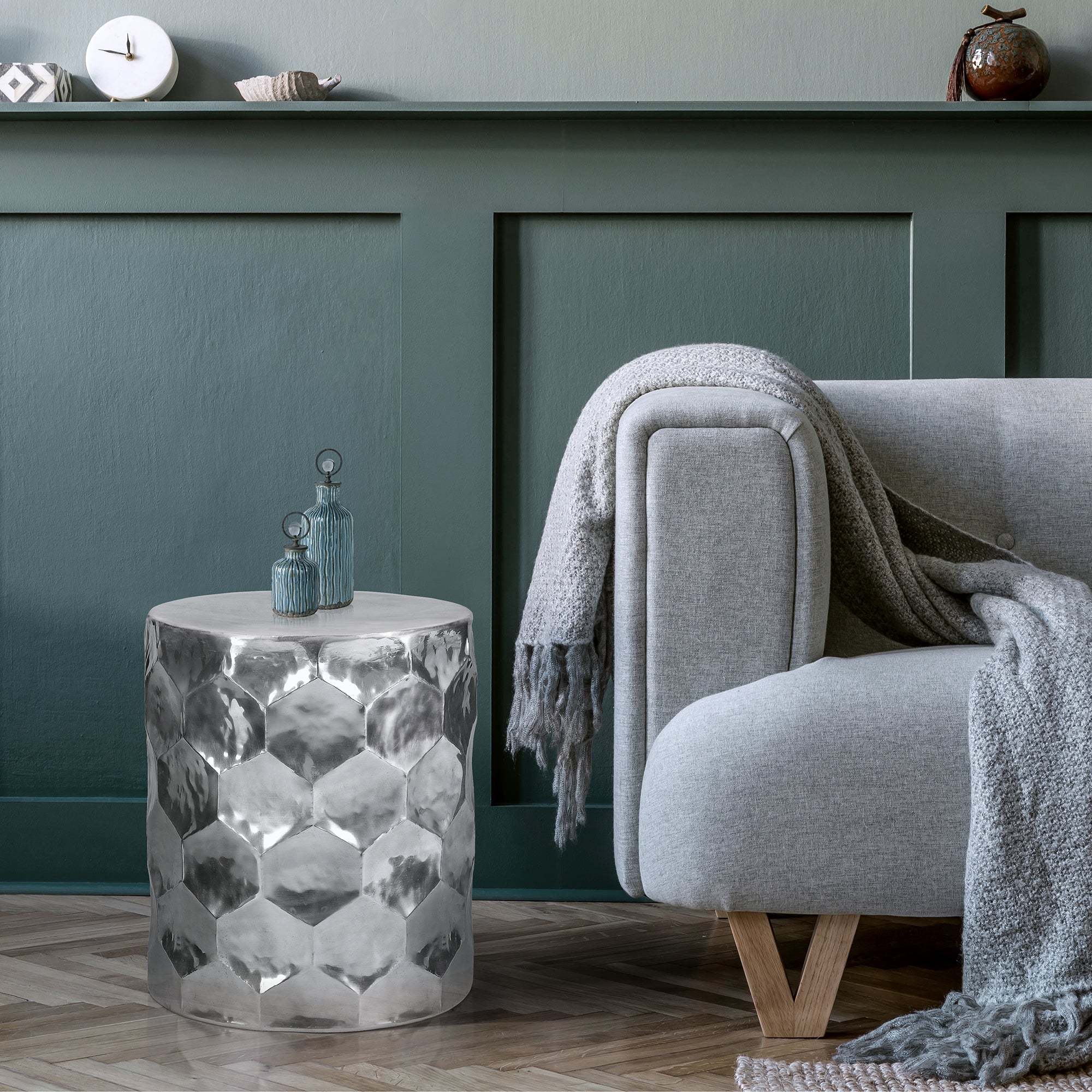 Gray sofa with a blanket and a round, silver table.